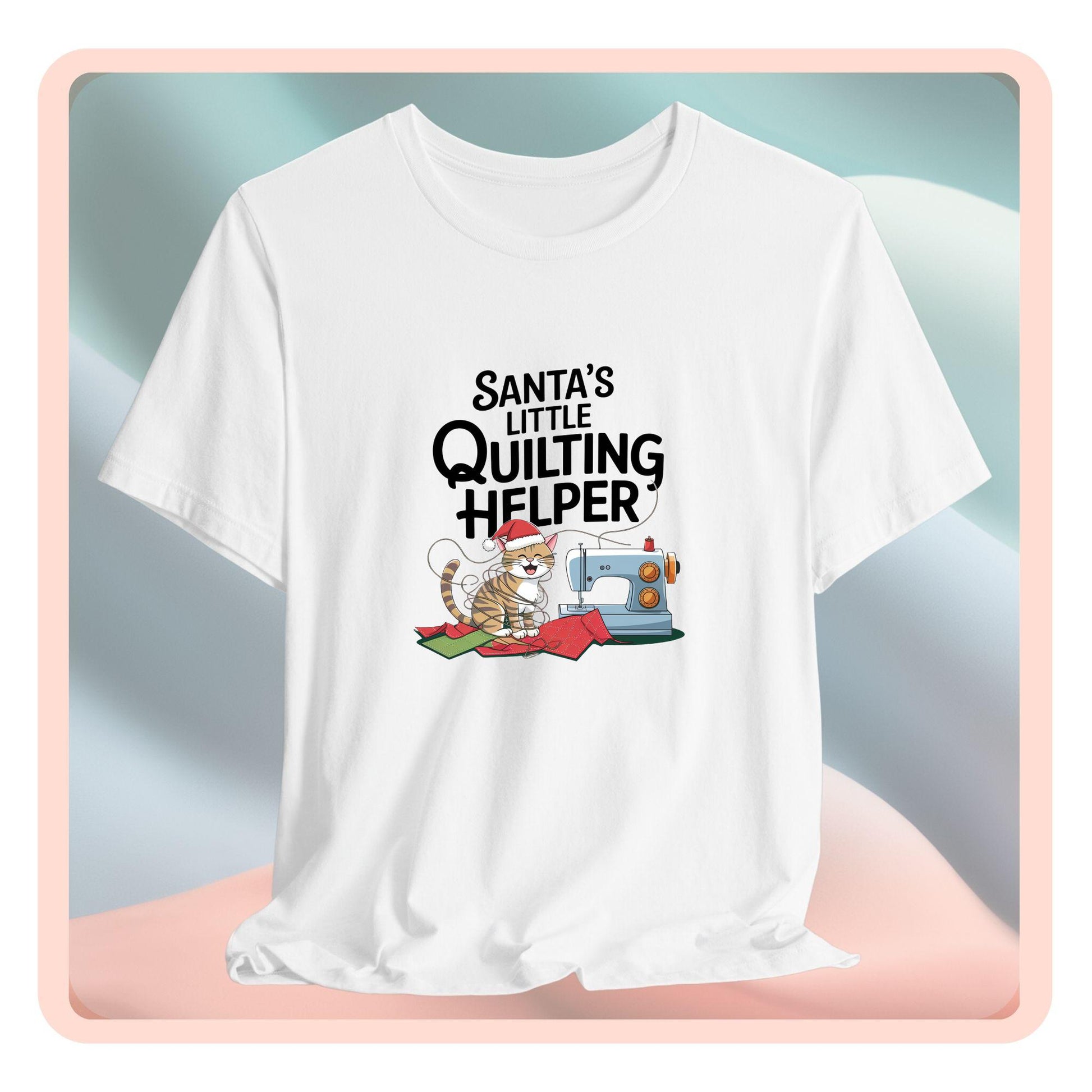 A christmas quilting t-shirt featuring a playful cat wearing a Santa hat is tangled in thread next to a sewing machine, with the phrase "Santa's Little Quilting Helper" above, combining quilting and holiday humor.