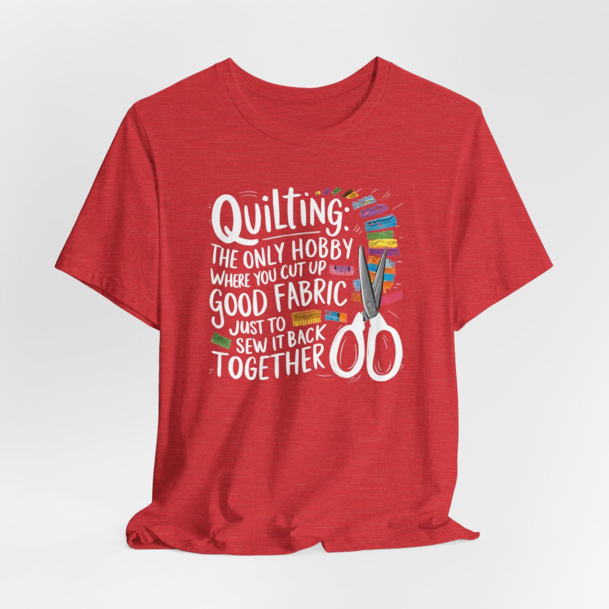 A Heather Red Quilting-themed T-Shirt with text "Quilting: The Only Hobby Where You Cut Up Good Fabric Just to Sew it Back Together" surrounded by colorful fabric scraps and scissors.