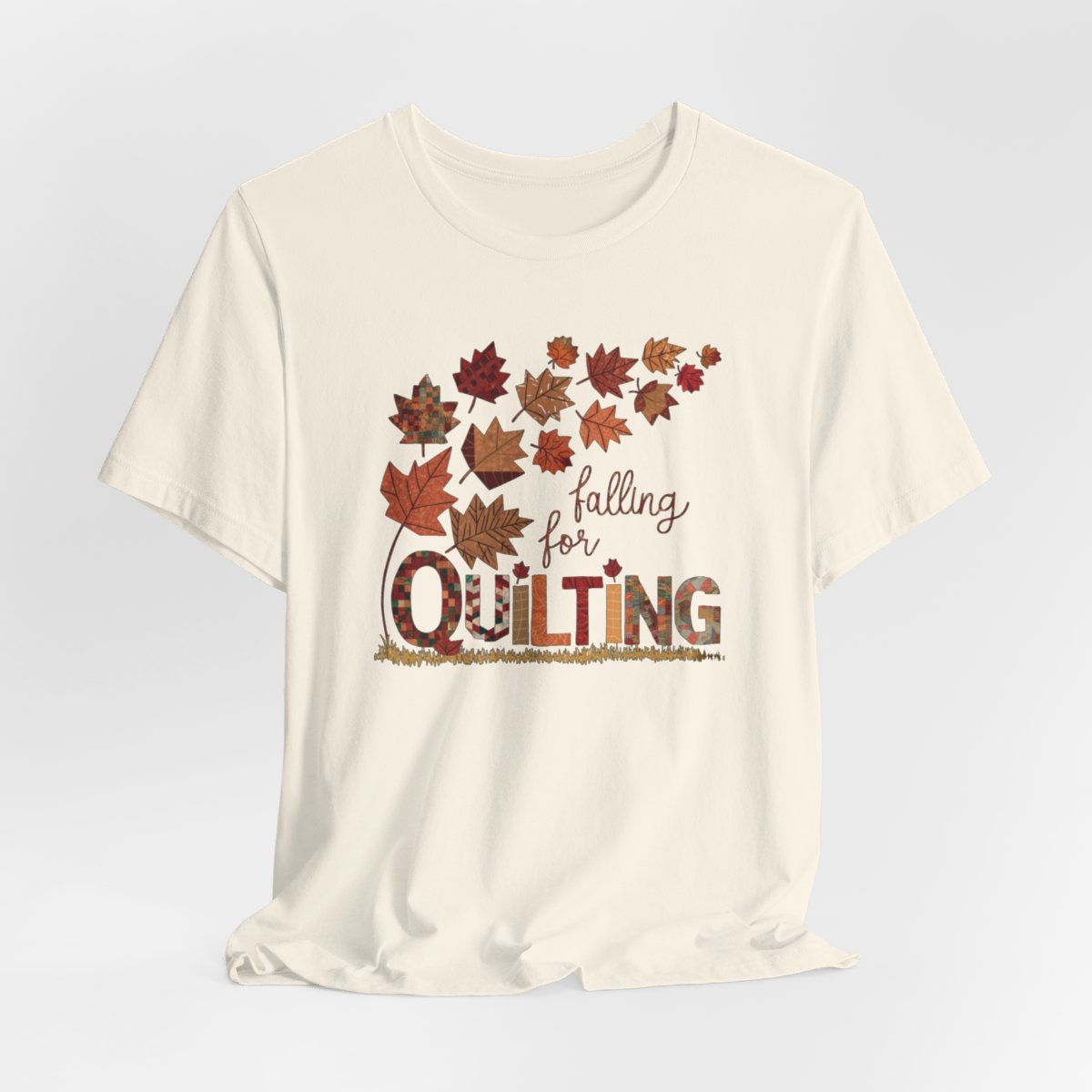 A Natural thanksgiving quilting t-shirt featuring autumn leaves with various quilting patterns inside. Text reads "falling for QUILTING" with letters in patchwork style. Warm fall colors and quilting motifs combine in a seasonal design.