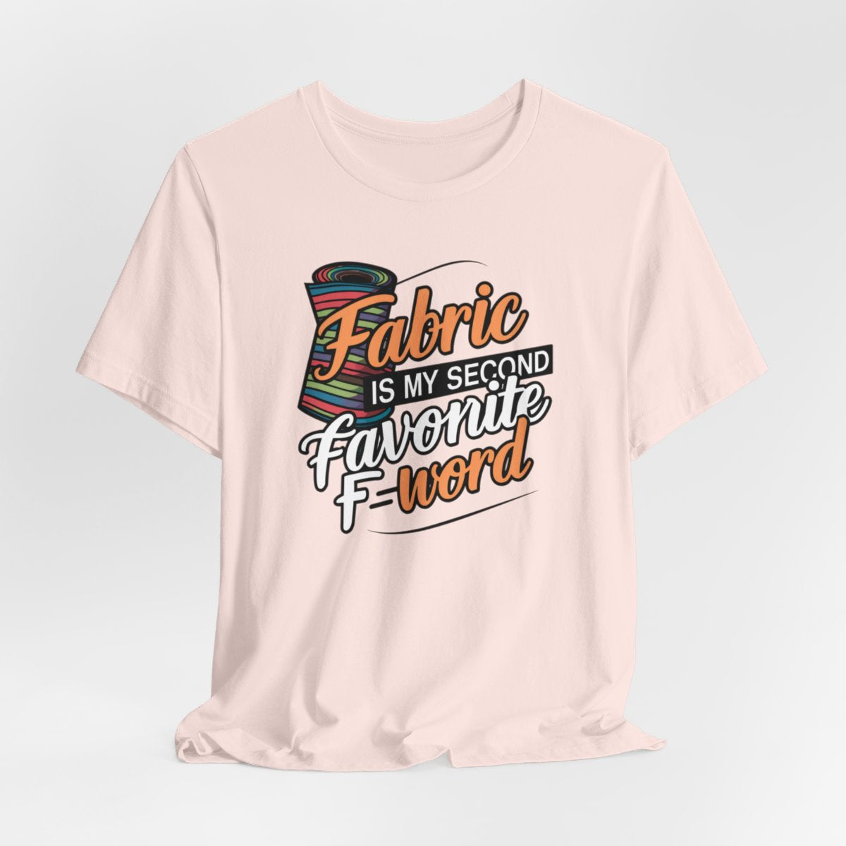 A Soft Pink T-Shirt with the phrase Fabric is My Second Favorite F-Word in a bold font next to a bolt of fabric