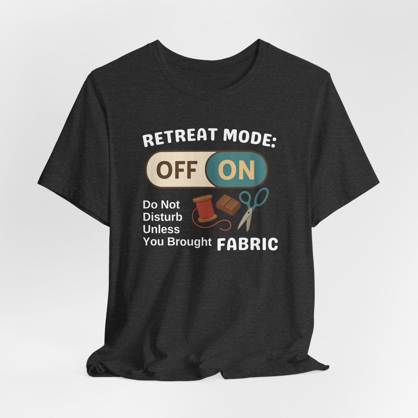 A A Dark Grey Heather t-shirt with a toggle switch that says "Retreat Mode: OFF/ON" surrounded by a spool of thread, chocolate, and scissors. Text below reads "Do not disturb unless you brought fabric." Fun gift for quilting retreats.
