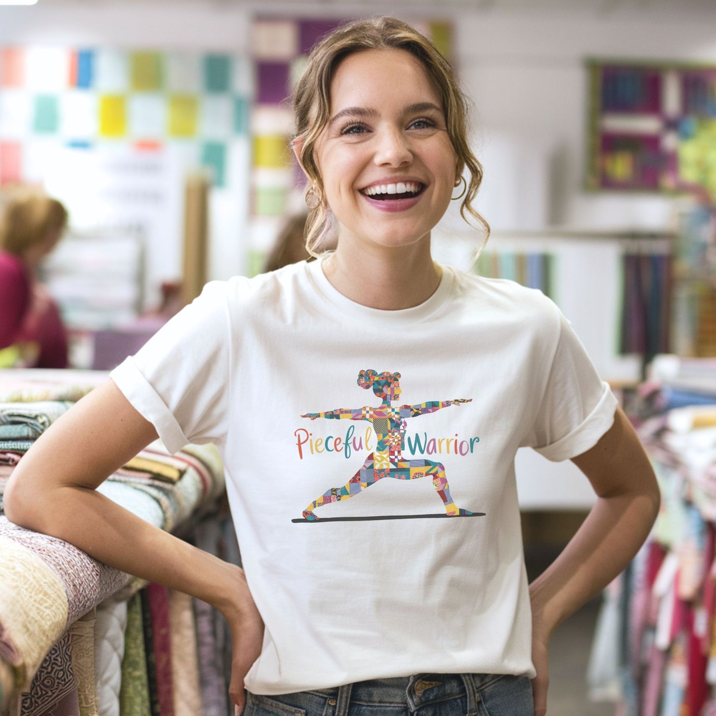 A Tee featuring a colorful patchwork silhouette of woman in yoga warrior pose. Text reads "Pieceful Warrior" in multicolored lettering.