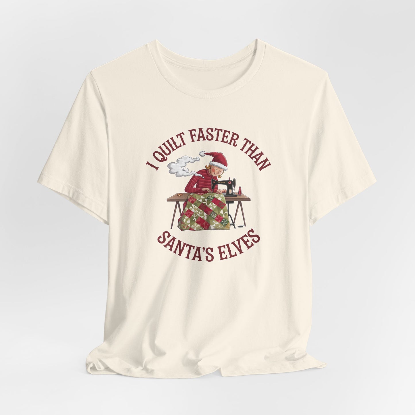 A Natural christmas quilting t-shirt featuring a quilter working at a sewing machine, quilting a festive holiday quilt, with the phrase "I Quilt Faster Than Santa's Elves" above the image, highlighting the speed and skill of the quilter.