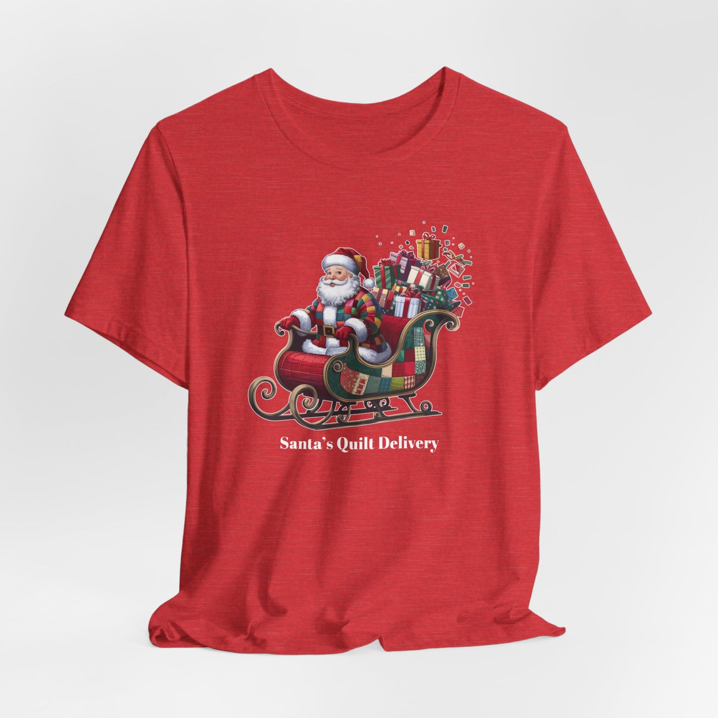 A Heather Red christmas quilting t-shirt featuring Santa Claus wearing a patchwork quilt coat, sitting in a sleigh filled with gifts and quilts, with the phrase "Santa's Quilt Delivery" below, combining holiday cheer and quilting fun.