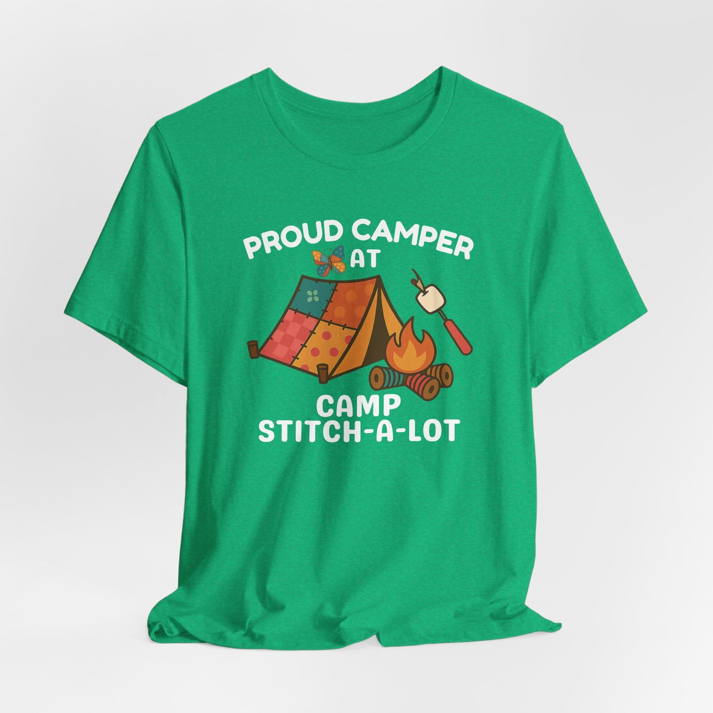A A Heather Kelly t-shirt featuring a colorful design with a patchwork tent, thread spool campfire, marshmallow on a seam ripper stick, and a butterfly. Text reads "Proud Camper at Camp Stitch-a-Lot." Fun gift for quilting retreats.