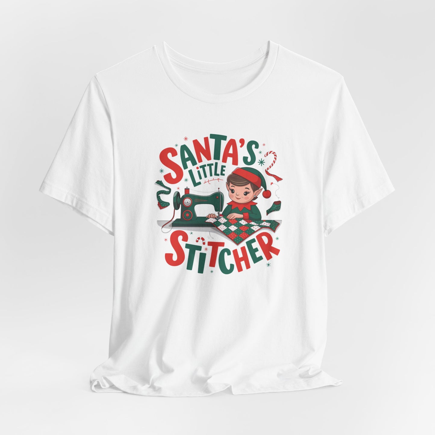 A White christmas quilting t-shirt featuring an adorable elf is sewing a festive patchwork quilt on a sewing machine, surrounded by holiday-themed decorations, with the phrase "Santa's Little Stitcher" above and below the design.