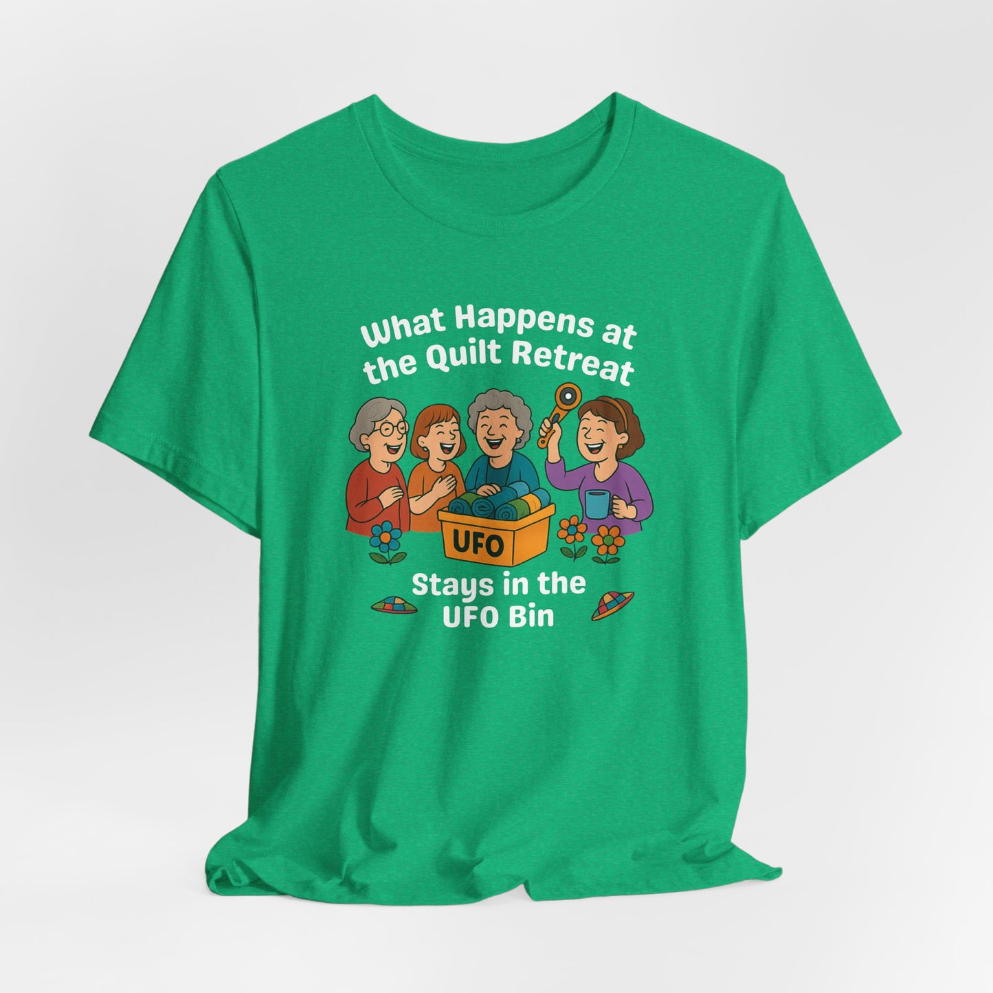 A A Heather Kelly t-shirt featuring a cartoon design of four laughing women at a quilt retreat with a bin labeled “UFO” full of fabric. Surrounded by patchwork flying saucers and flowers. Text reads “What happens at the quilt retreat stays in the UFO bin.”