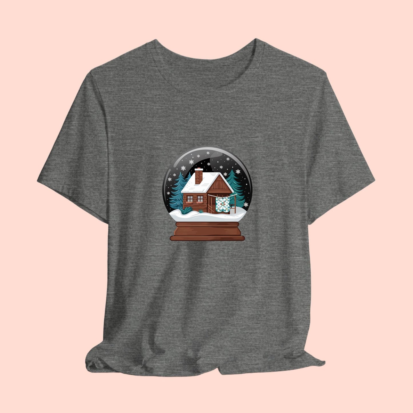 A christmas quilting t-shirt featuring a cozy log cabin covered in snow, with a quilt hanging outside, set inside a snow globe with swirling snowflakes, blending quilting and holiday warmth.