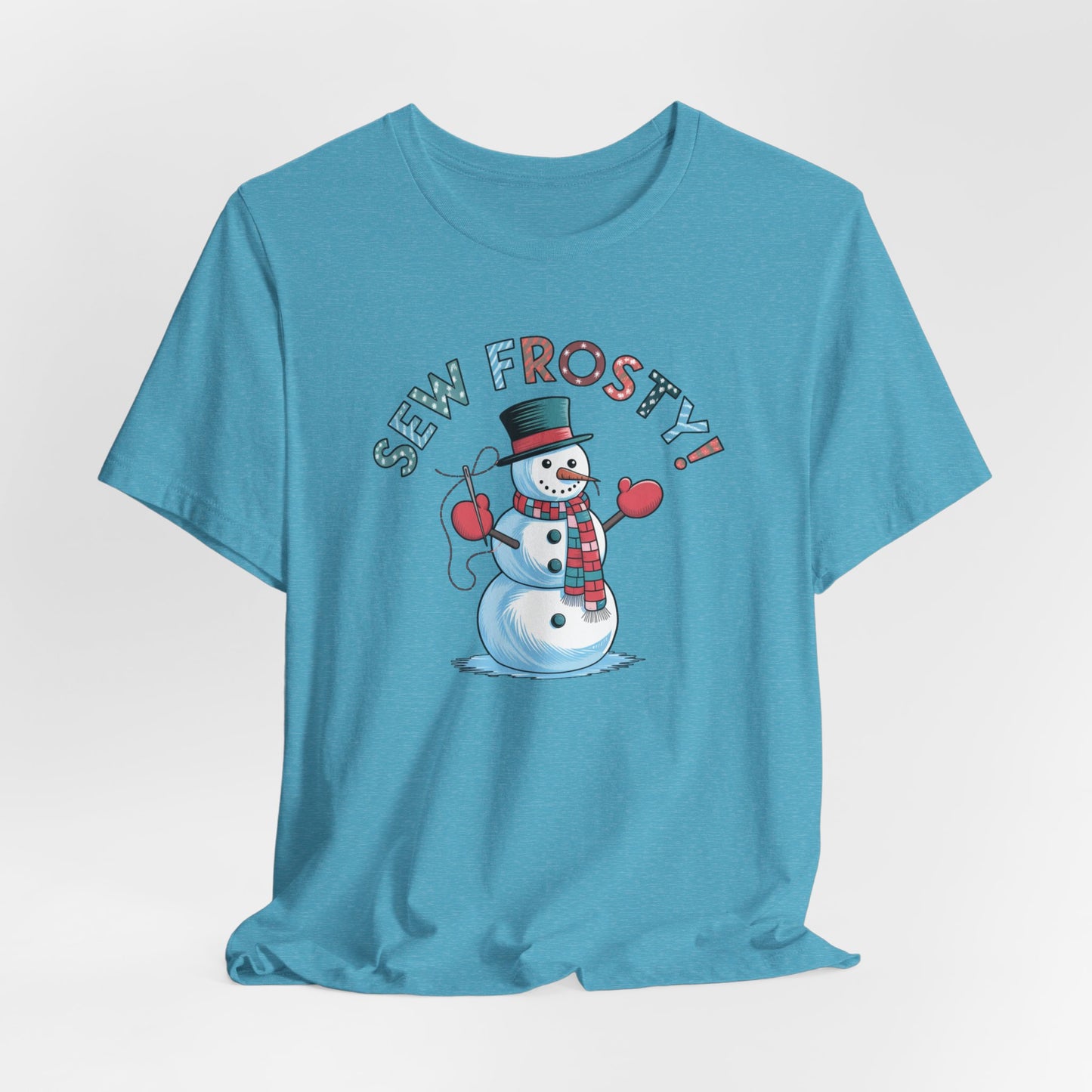 A Heather Aqua christmas quilting t-shirt featuring cheerful snowman design holding a sewing needle, with the phrase "Sew Frosty" in playful, winter-themed lettering. The snowman is wearing a scarf and mittens, ready for holiday sewing fun.