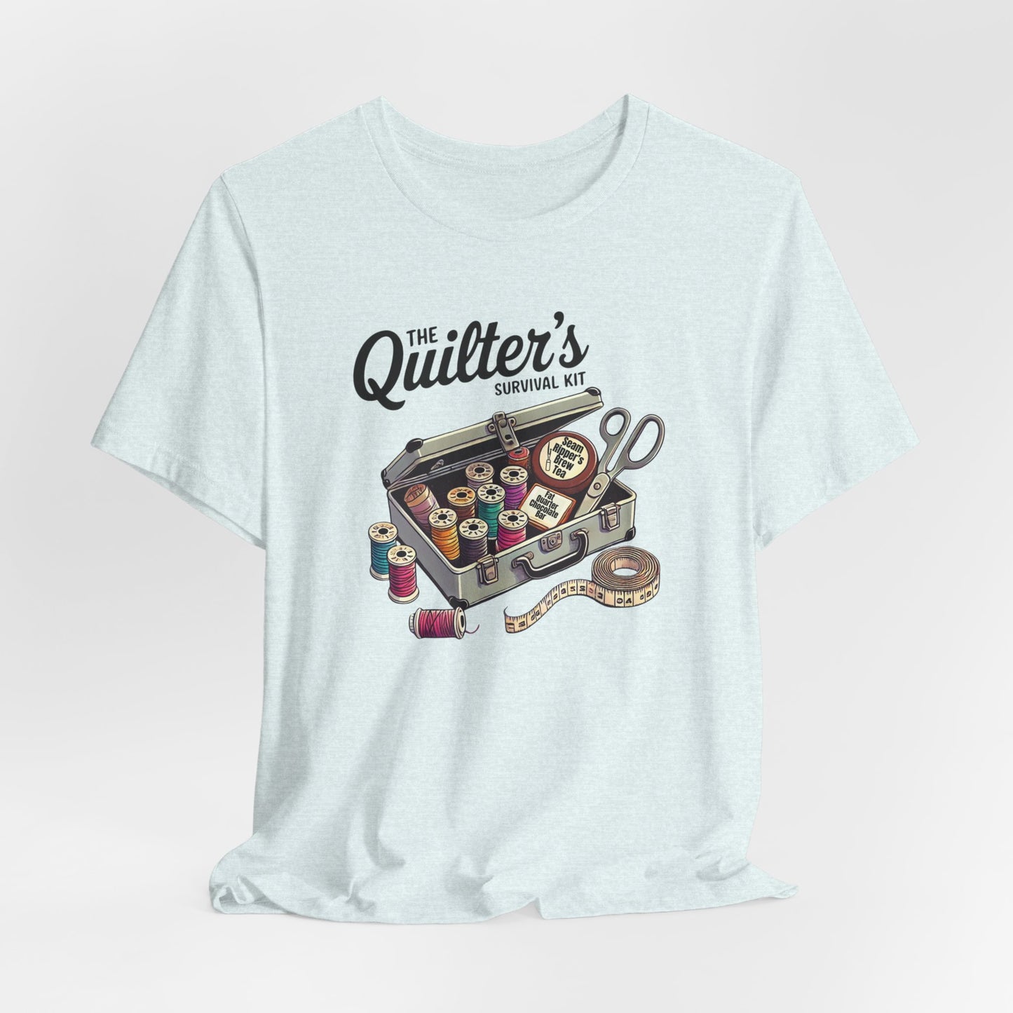 A Heather Ice Blue t-shirt featuring a whimsical illustration of a quilter’s survival kit with colorful thread spools, scissors, and a tape measure, perfect for sewing and quilting enthusiasts.