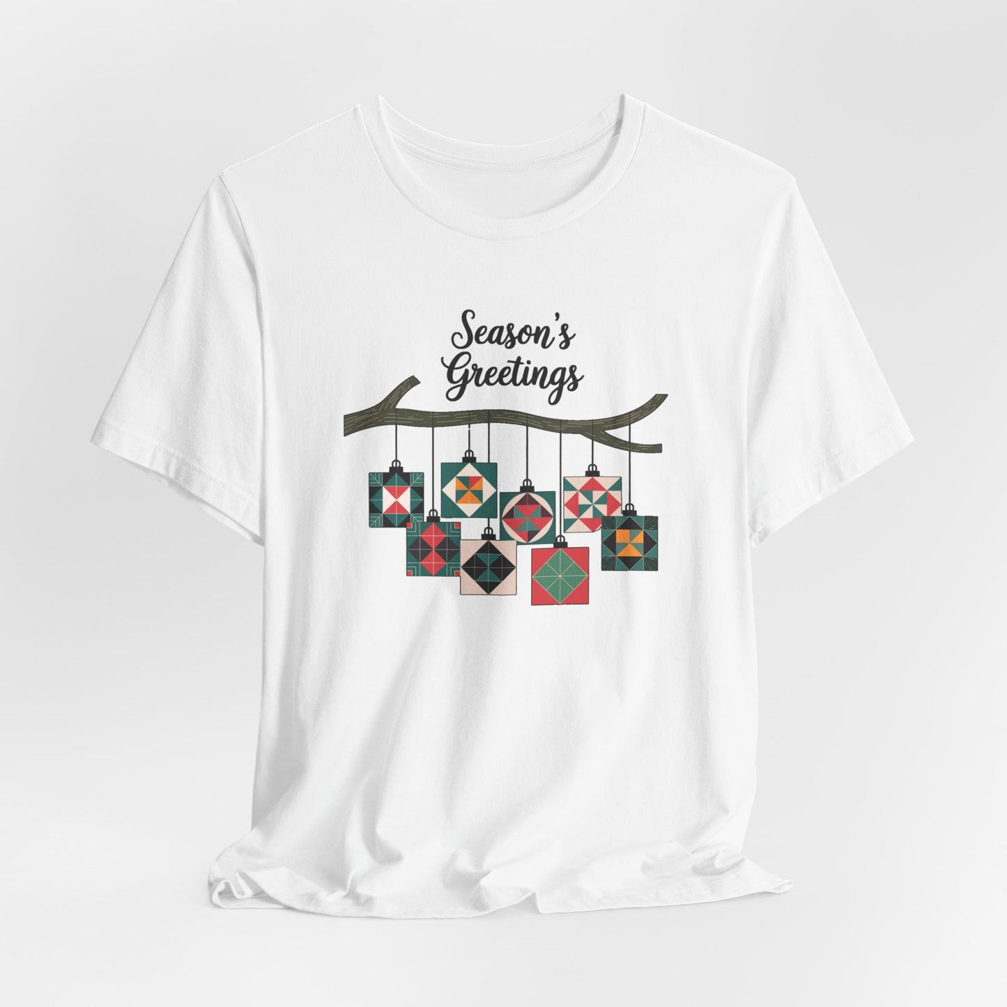 A White christmas quilting t-shirt featuring quilt block ornaments hanging from a branch, featuring the phrase "Season's Greetings" above. The ornaments showcase various quilting patterns to highlight the holiday quilting theme.