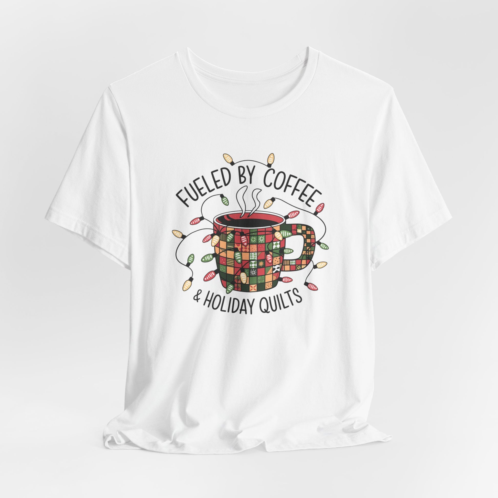 A White christmas quilting t-shirt featuring a cozy coffee mug covered in patchwork quilt patterns, wrapped in festive holiday lights, with the phrase "Fueled by Coffee & Holiday Quilts" surrounding the design.