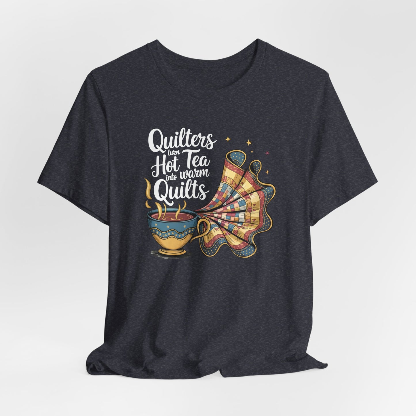 A Heather Navy t-shirt with a whimsical design of a teacup transforming into a patchwork quilt, accompanied by the phrase 'Quilters turn hot tea into warm quilts.' Ideal for quilters and tea lovers