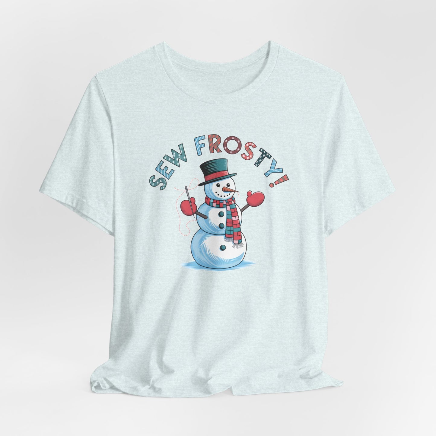 A Heather Ice Blue christmas quilting t-shirt featuring cheerful snowman design holding a sewing needle, with the phrase "Sew Frosty" in playful, winter-themed lettering. The snowman is wearing a scarf and mittens, ready for holiday sewing fun.