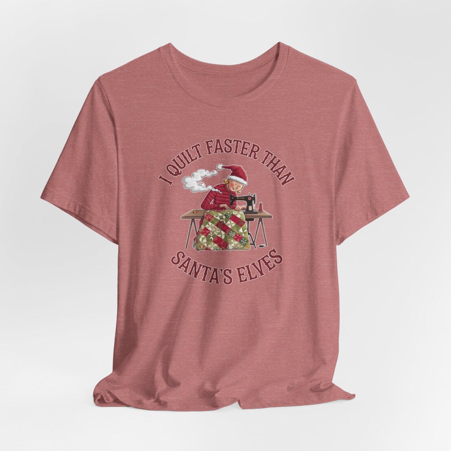 A Heather Mauve christmas quilting t-shirt featuring a quilter working at a sewing machine, quilting a festive holiday quilt, with the phrase "I Quilt Faster Than Santa's Elves" above the image, highlighting the speed and skill of the quilter.