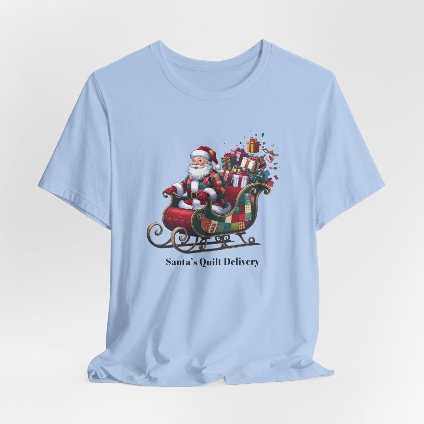 A Baby Blue christmas quilting t-shirt featuring Santa Claus wearing a patchwork quilt coat, sitting in a sleigh filled with gifts and quilts, with the phrase "Santa's Quilt Delivery" below, combining holiday cheer and quilting fun.