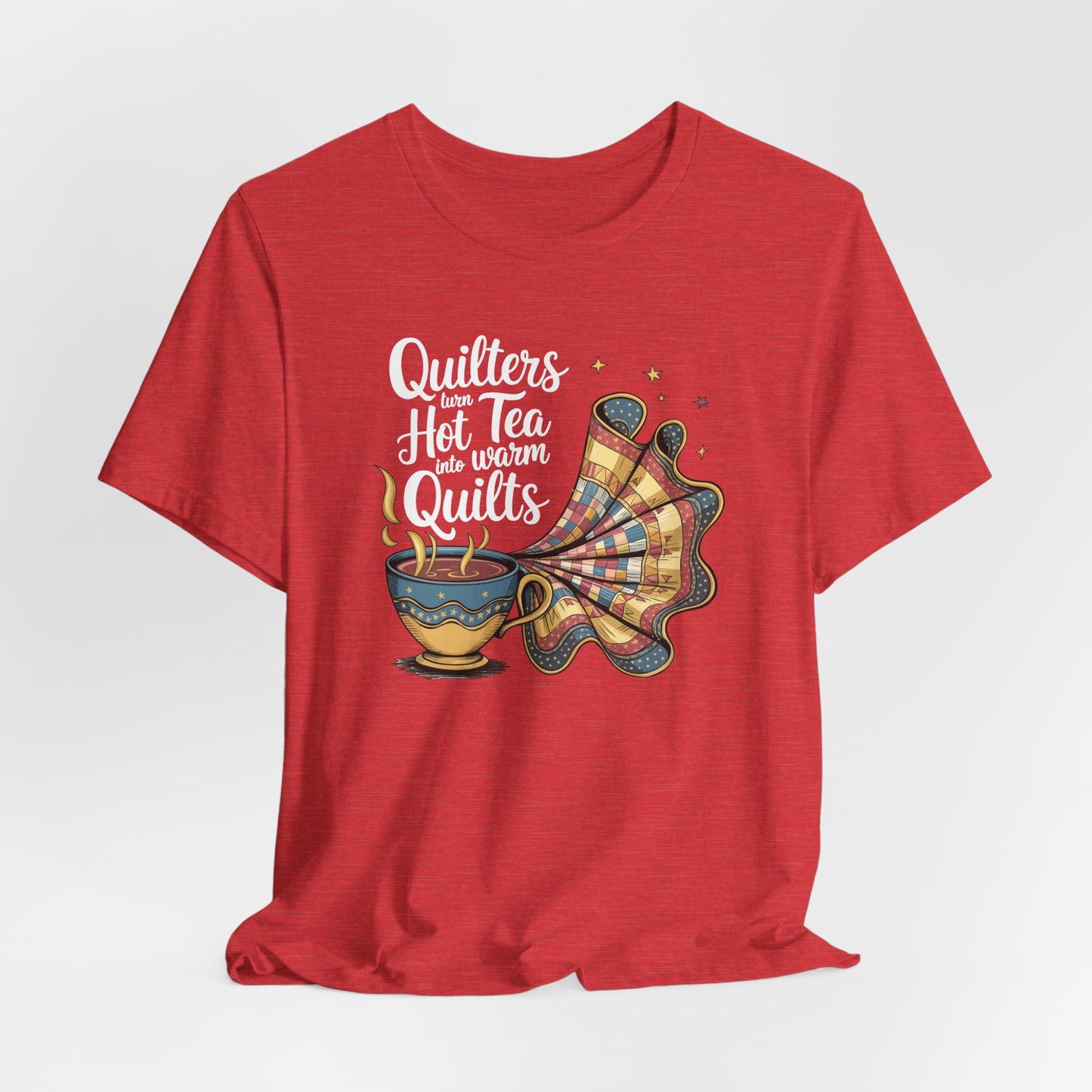 A Heather Red t-shirt with a whimsical design of a teacup transforming into a patchwork quilt, accompanied by the phrase 'Quilters turn hot tea into warm quilts.' Ideal for quilters and tea lovers