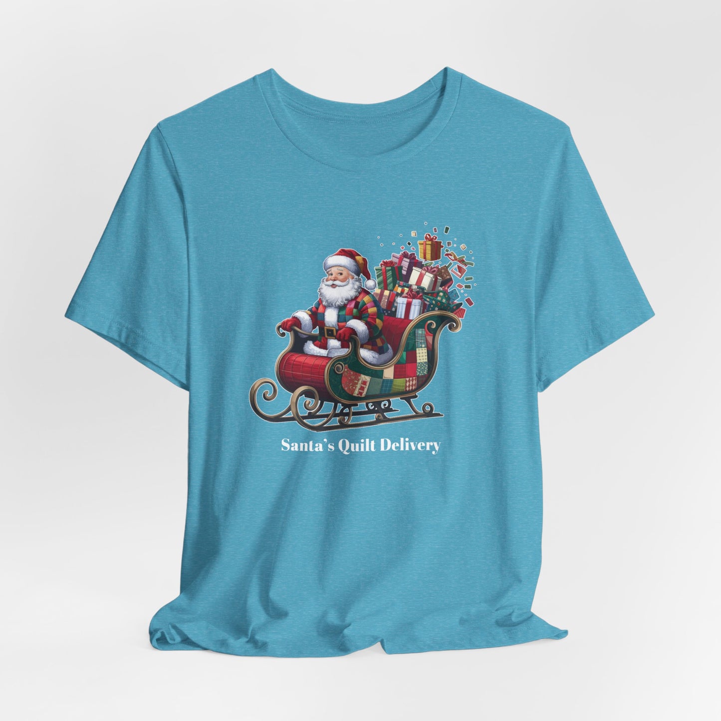 A Heather Aqua christmas quilting t-shirt featuring Santa Claus wearing a patchwork quilt coat, sitting in a sleigh filled with gifts and quilts, with the phrase "Santa's Quilt Delivery" below, combining holiday cheer and quilting fun.