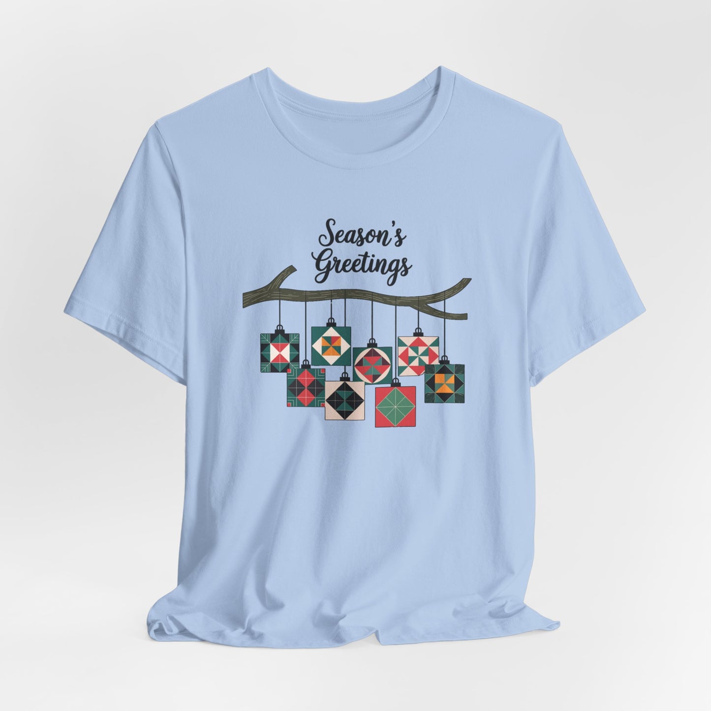 A Baby Blue christmas quilting t-shirt featuring quilt block ornaments hanging from a branch, featuring the phrase "Season's Greetings" above. The ornaments showcase various quilting patterns to highlight the holiday quilting theme.