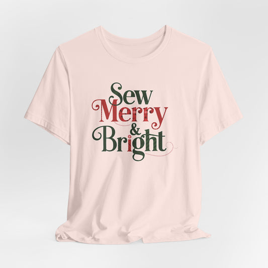A Soft Pink t-shirt with the phrase "Sew Merry & Bright," incorporating sewing-inspired elements and holiday-themed accents, such as stitching lines and festive patterns.