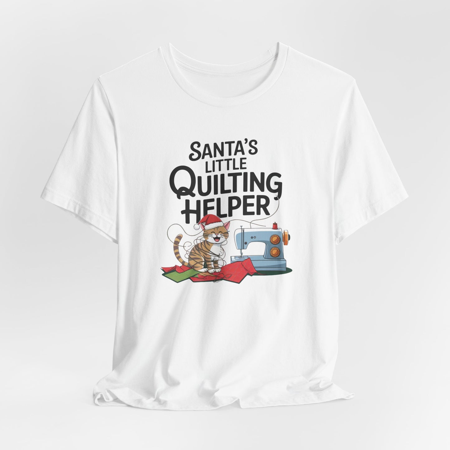 A White christmas quilting t-shirt featuring a playful cat wearing a Santa hat is tangled in thread next to a sewing machine, with the phrase "Santa's Little Quilting Helper" above, combining quilting and holiday humor.