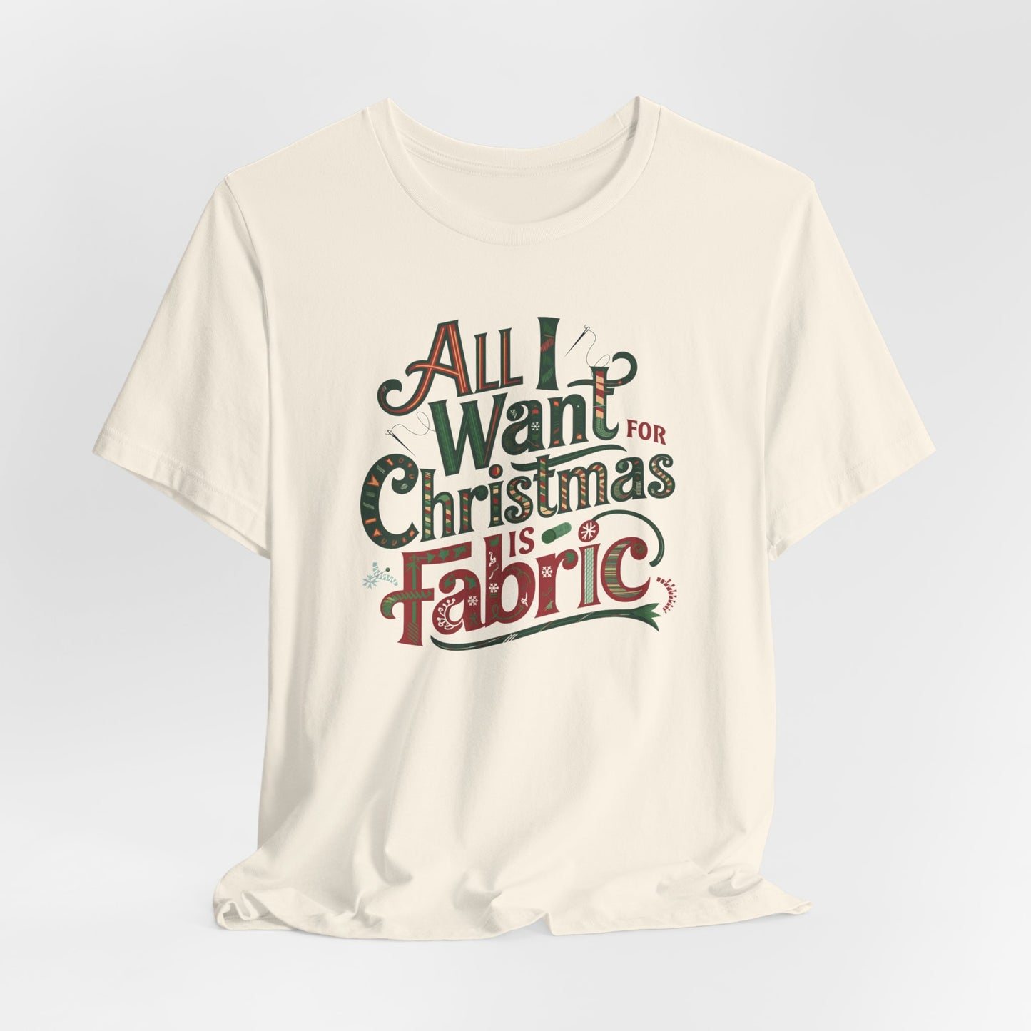 A Natural festive quilting christmas T-shirt featuring the phrase "All I Want for Christmas is Fabric," with fun sewing and quilting accents like needles and threads swirling around the text.