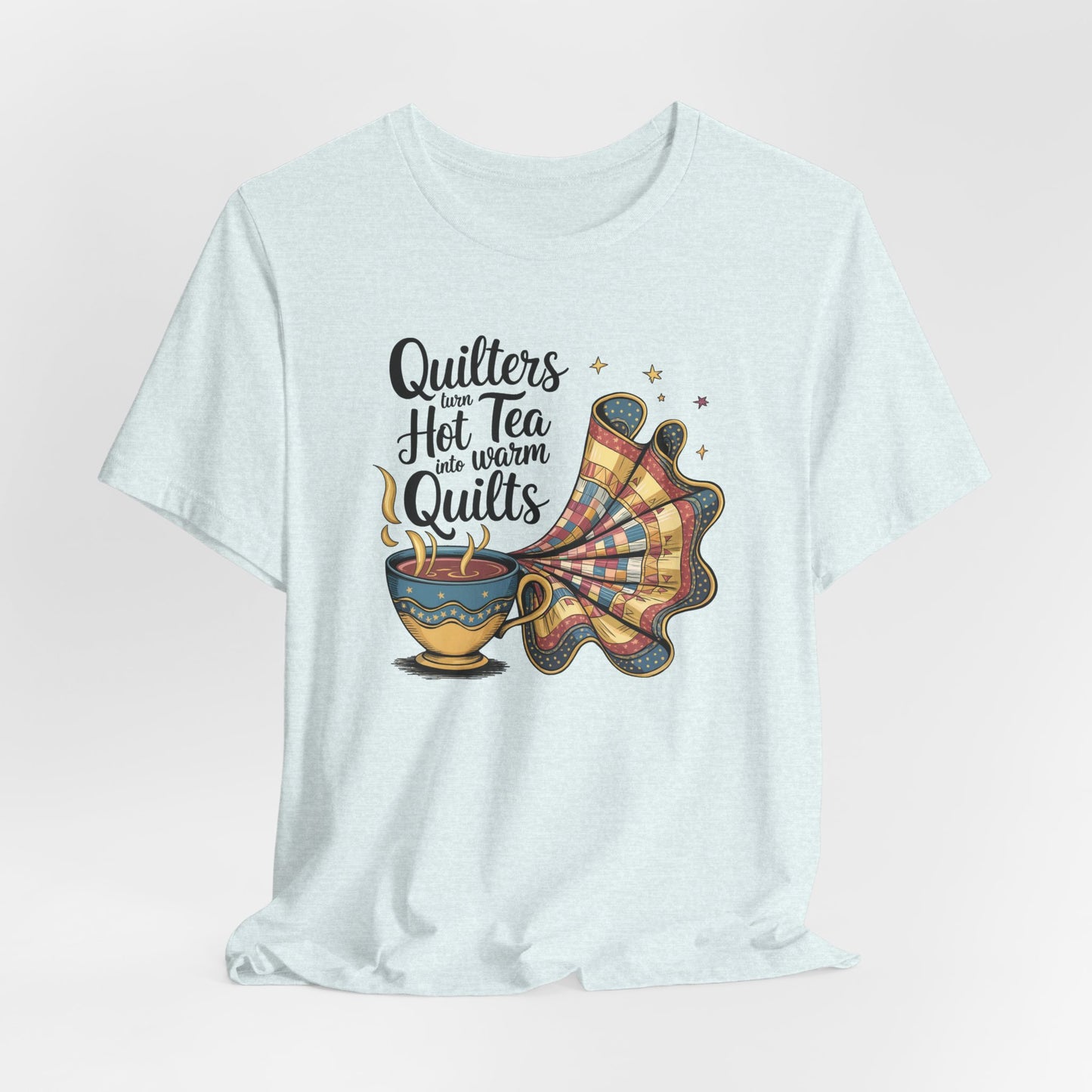 A Heather Ice Blue t-shirt with a whimsical design of a teacup transforming into a patchwork quilt, accompanied by the phrase 'Quilters turn hot tea into warm quilts.' Ideal for quilters and tea lovers