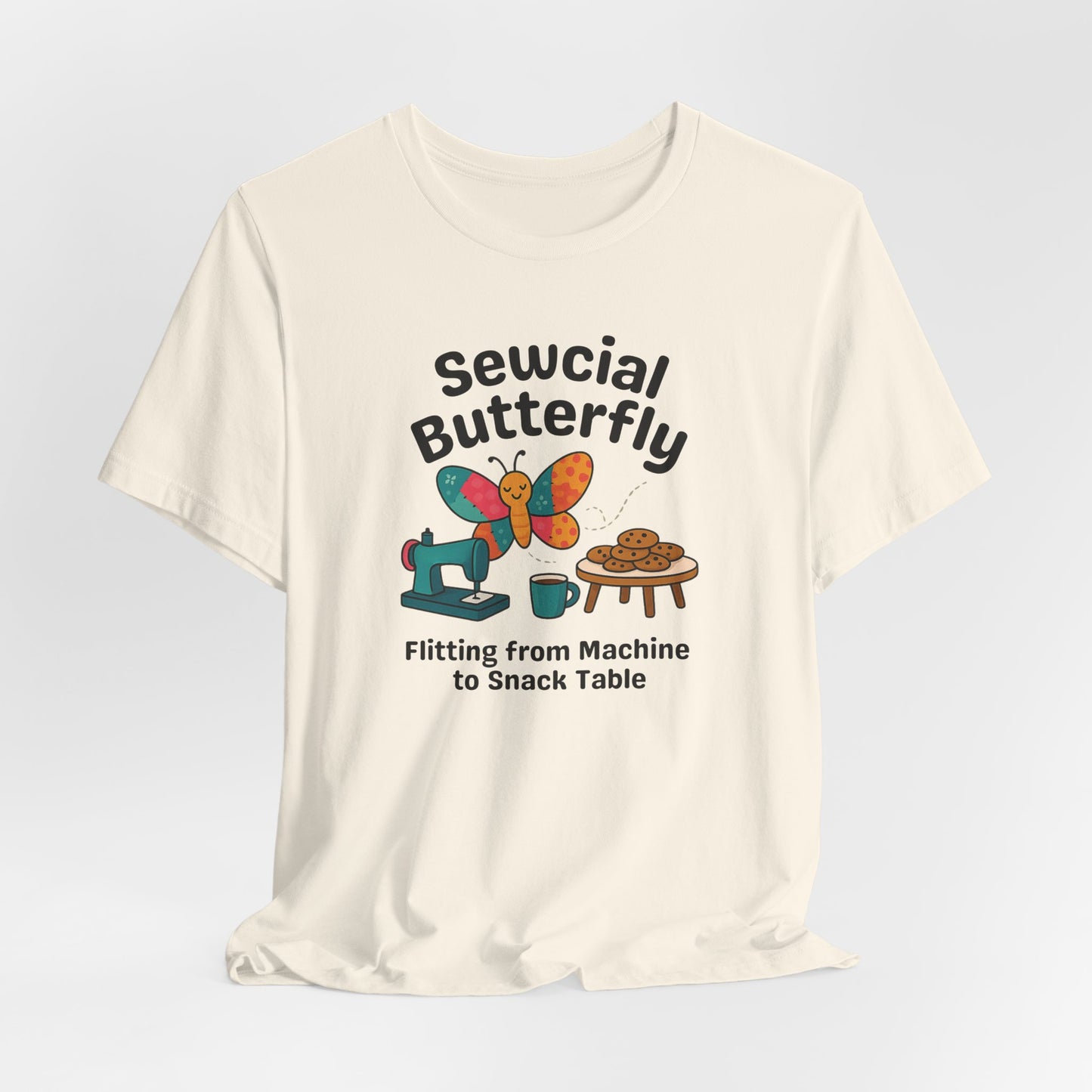A A Natural t-shirt with a colorful design showing a patchwork butterfly flying between a sewing machine and a table of cookies. Text reads “Sewcial Butterfly – Flitting from Machine to Snack Table.” Funny gift for quilters