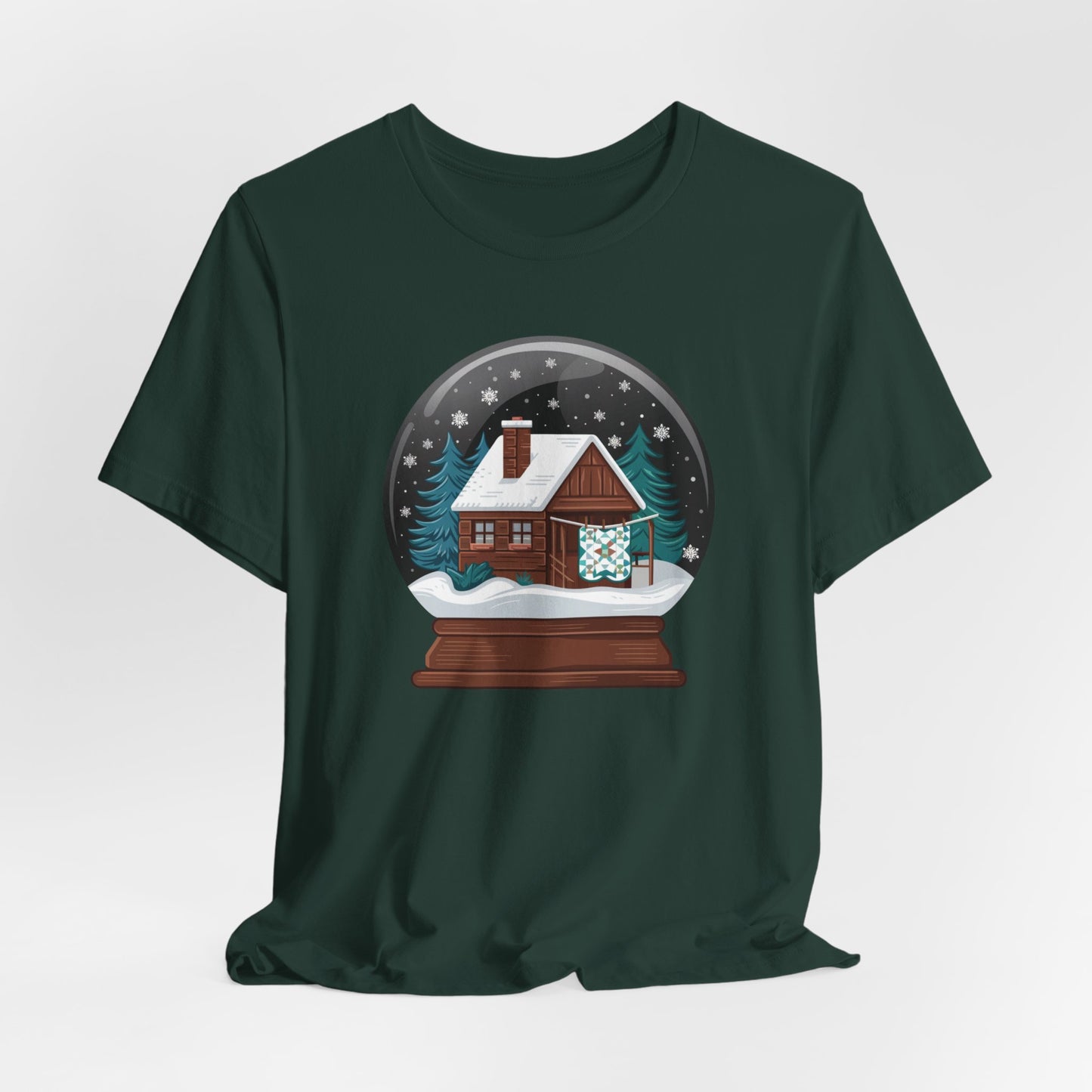 A Forest christmas quilting t-shirt featuring a cozy log cabin covered in snow, with a quilt hanging outside, set inside a snow globe with swirling snowflakes, blending quilting and holiday warmth.