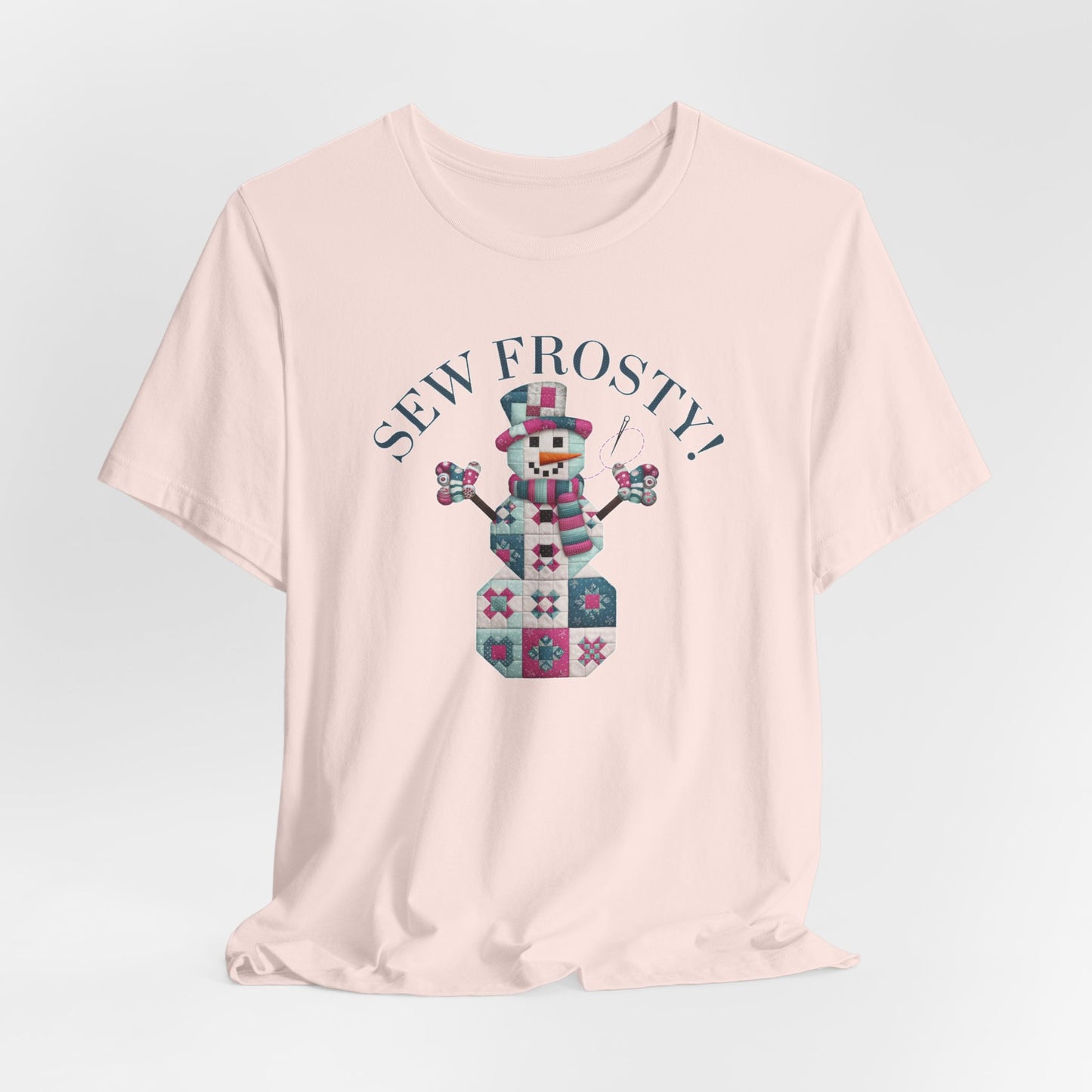 A Soft Pink christmas quilting t-shirt featuring cute snowman made of patchwork quilt blocks with the phrase "Sew Frosty" above, holding a needle to highlight the quilting theme.