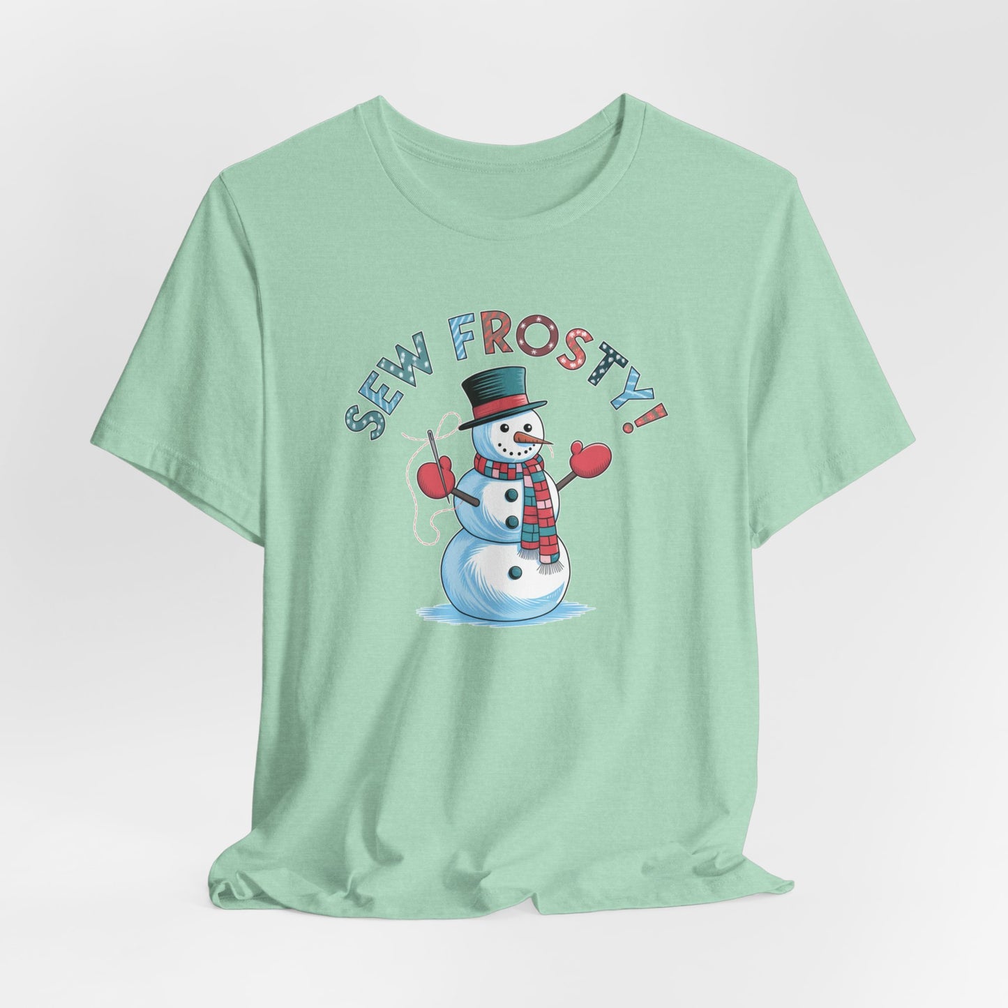 A Heather Mint christmas quilting t-shirt featuring cheerful snowman design holding a sewing needle, with the phrase "Sew Frosty" in playful, winter-themed lettering. The snowman is wearing a scarf and mittens, ready for holiday sewing fun.