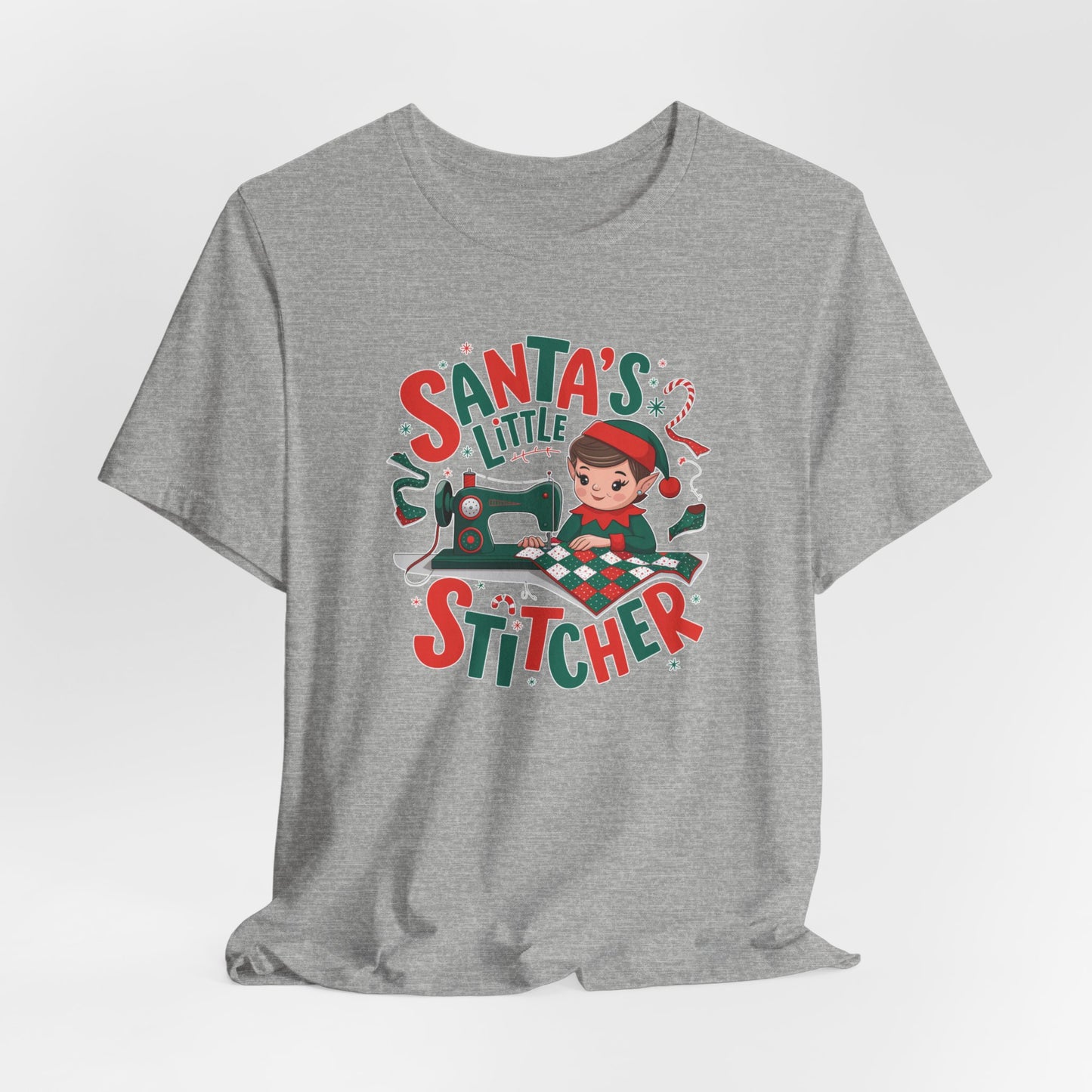 An Athletic Heather christmas quilting t-shirt featuring an adorable elf is sewing a festive patchwork quilt on a sewing machine, surrounded by holiday-themed decorations, with the phrase "Santa's Little Stitcher" above and below the design.