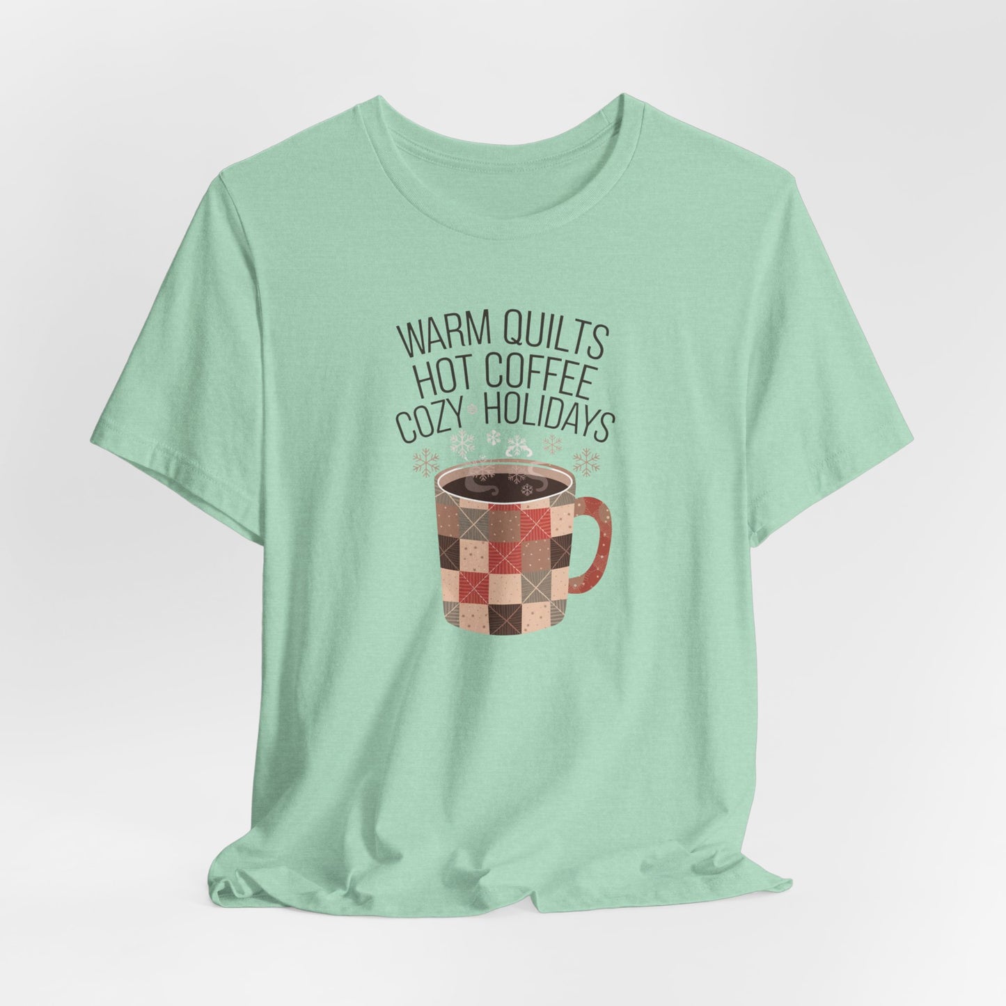 A Heather Mint christmas quilting t-shirt featuring a cozy patchwork quilt-themed coffee mug, surrounded by snowflakes, with the phrase "Warm Quilts, Hot Coffee, Cozy Holidays" above the mug, celebrating the warmth of quilts and coffee during the holiday season.