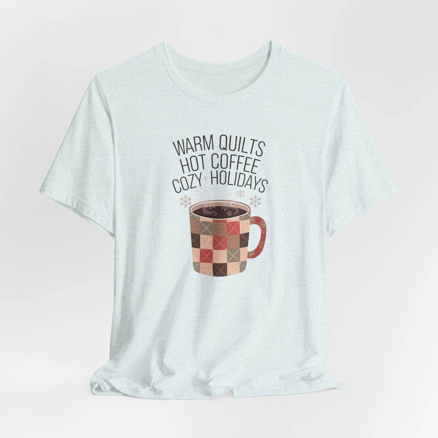 A Heather Ice Blue christmas quilting t-shirt featuring a cozy patchwork quilt-themed coffee mug, surrounded by snowflakes, with the phrase "Warm Quilts, Hot Coffee, Cozy Holidays" above the mug, celebrating the warmth of quilts and coffee during the holiday season.