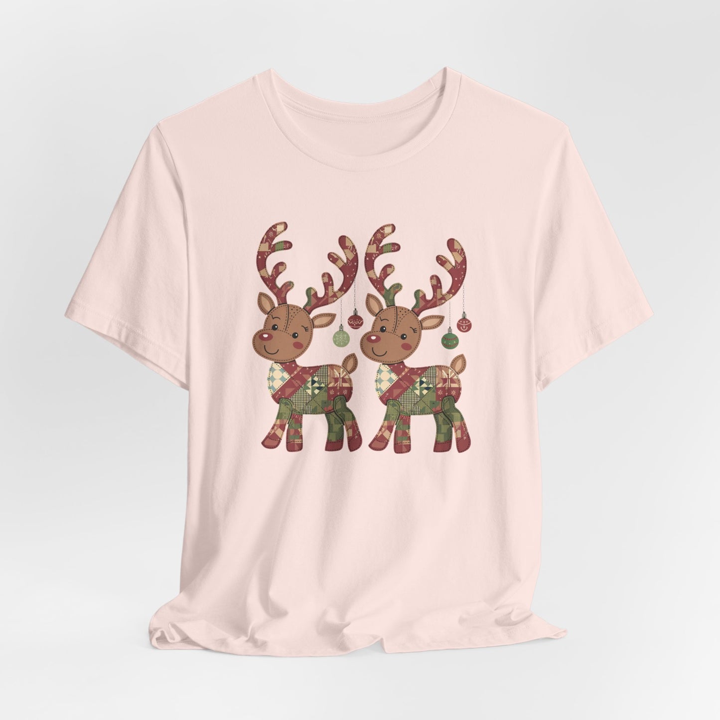 A Soft Pink christmas quilting t-shirt featuring two adorable reindeer featuring patchwork quilt designs on their bodies, with ornaments hanging from their antlers, blending Christmas cheer with quilting creativity.