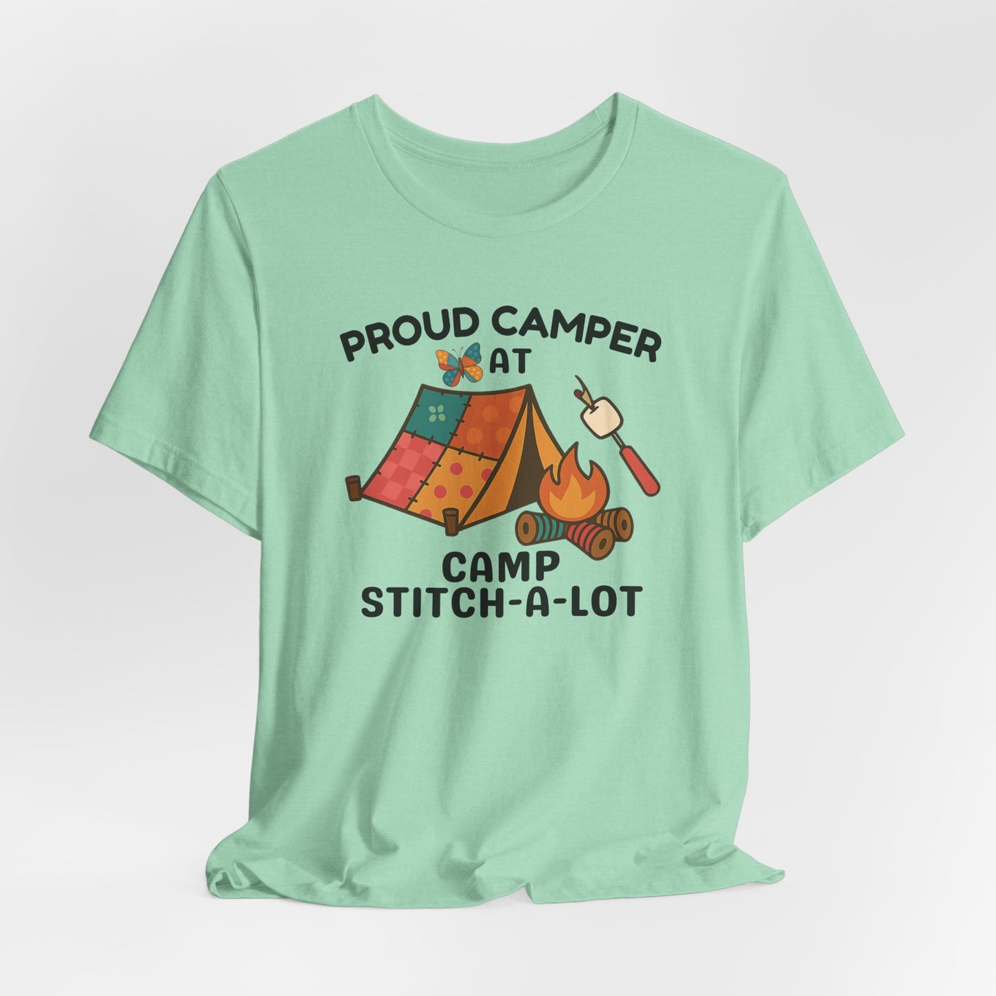A A Heather Mint t-shirt featuring a colorful design with a patchwork tent, thread spool campfire, marshmallow on a seam ripper stick, and a butterfly. Text reads "Proud Camper at Camp Stitch-a-Lot." Fun gift for quilting retreats.