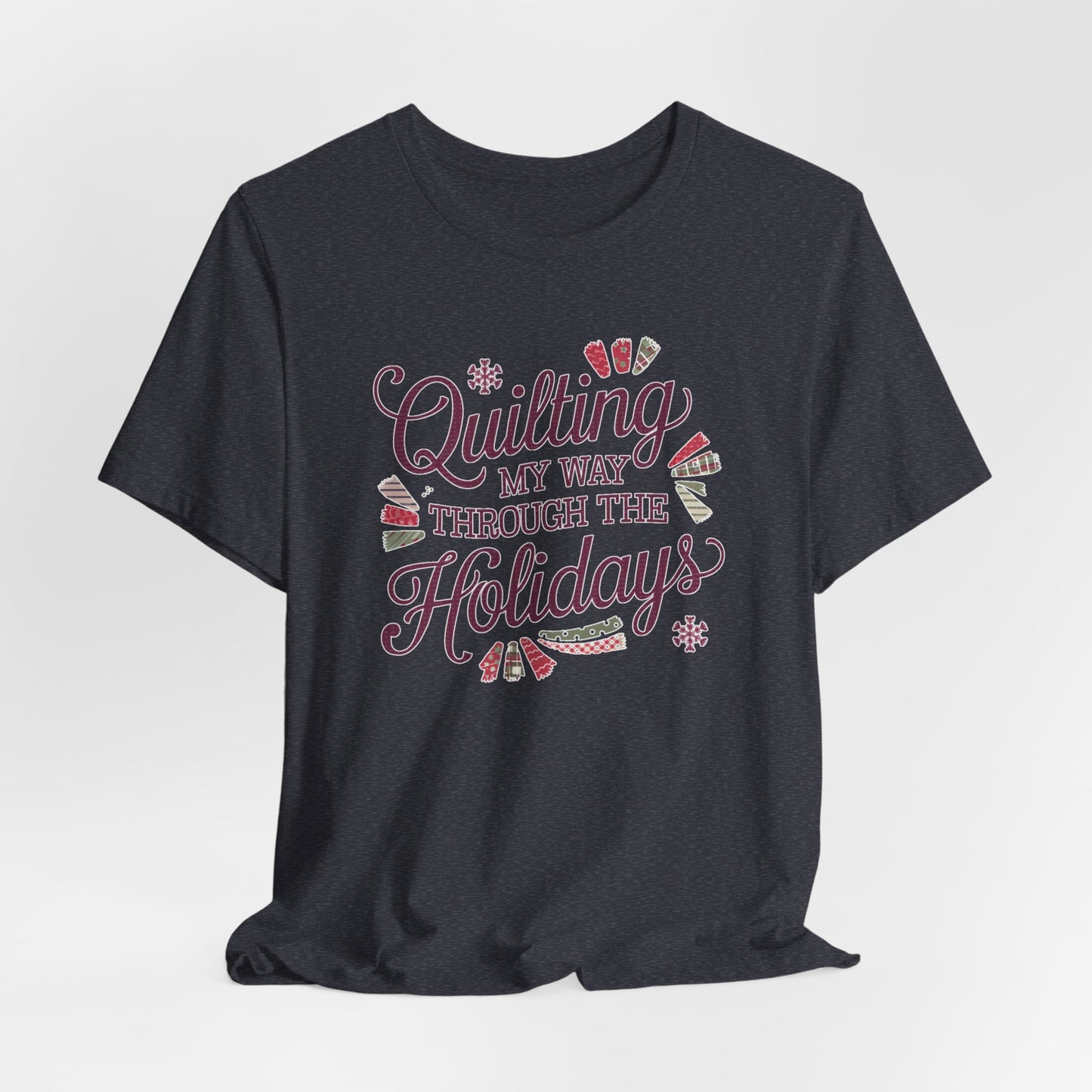 A Heather Navy playful holiday-themed t-shirt with the phrase "Quilting My Way Through the Holidays" surrounded by quilting-inspired decorations like fabric swatches and snowflakes.