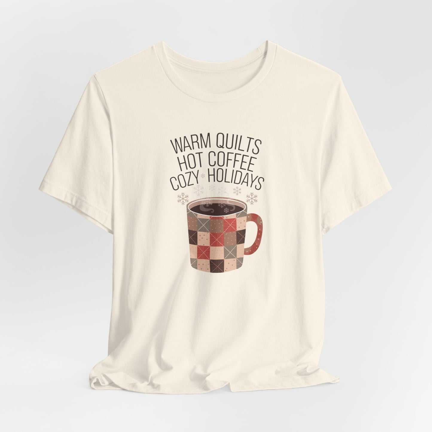 A Natural christmas quilting t-shirt featuring a cozy patchwork quilt-themed coffee mug, surrounded by snowflakes, with the phrase "Warm Quilts, Hot Coffee, Cozy Holidays" above the mug, celebrating the warmth of quilts and coffee during the holiday season.