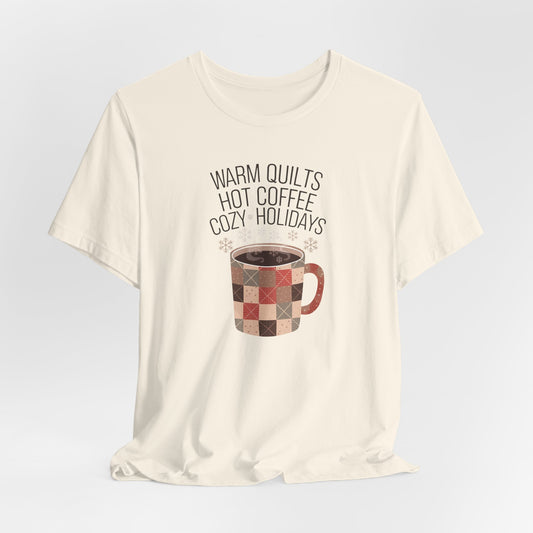 A Natural christmas quilting t-shirt featuring a cozy patchwork quilt-themed coffee mug, surrounded by snowflakes, with the phrase "Warm Quilts, Hot Coffee, Cozy Holidays" above the mug, celebrating the warmth of quilts and coffee during the holiday season.
