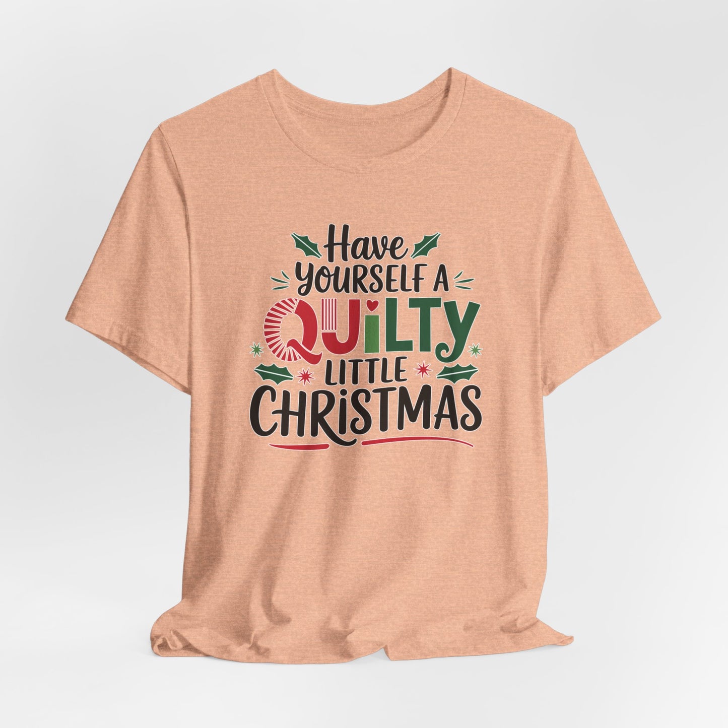A Heather Peach fun holiday-themed t-shirt featuring the phrase "Have Yourself a Quilty Little Christmas" with quilting-inspired elements and holiday decorations such as holly and stars.
