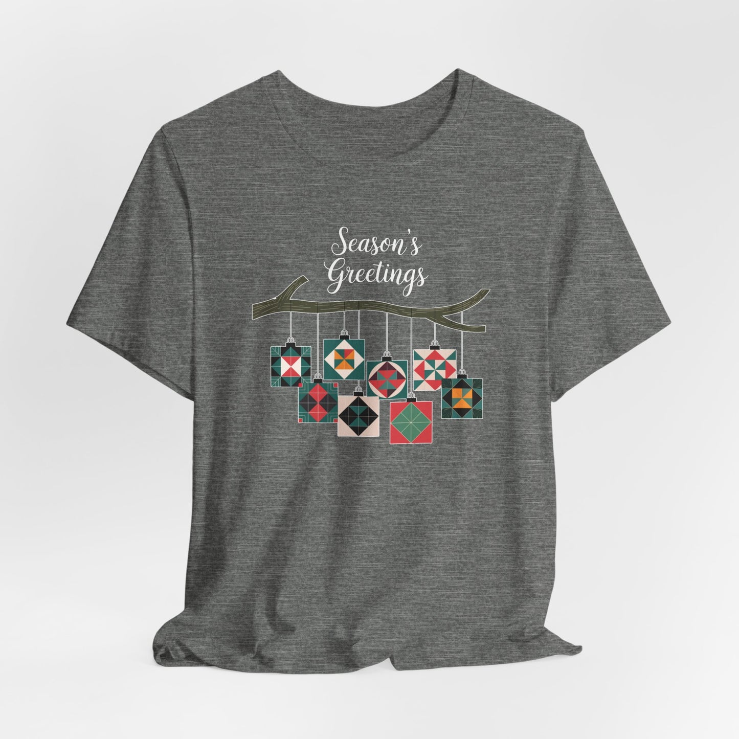 A Deep Heather christmas quilting t-shirt featuring quilt block ornaments hanging from a branch, featuring the phrase "Season's Greetings" above. The ornaments showcase various quilting patterns to highlight the holiday quilting theme.