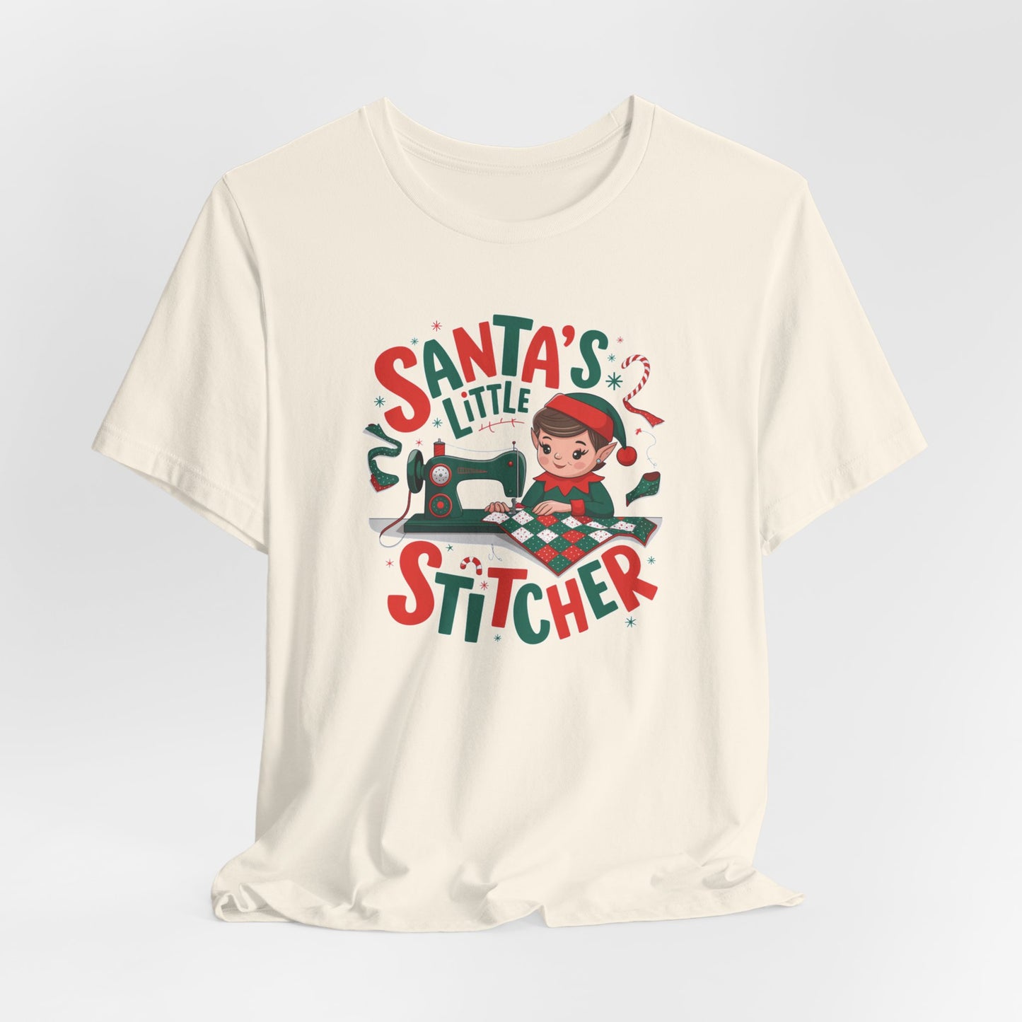 A Natural christmas quilting t-shirt featuring an adorable elf is sewing a festive patchwork quilt on a sewing machine, surrounded by holiday-themed decorations, with the phrase "Santa's Little Stitcher" above and below the design.