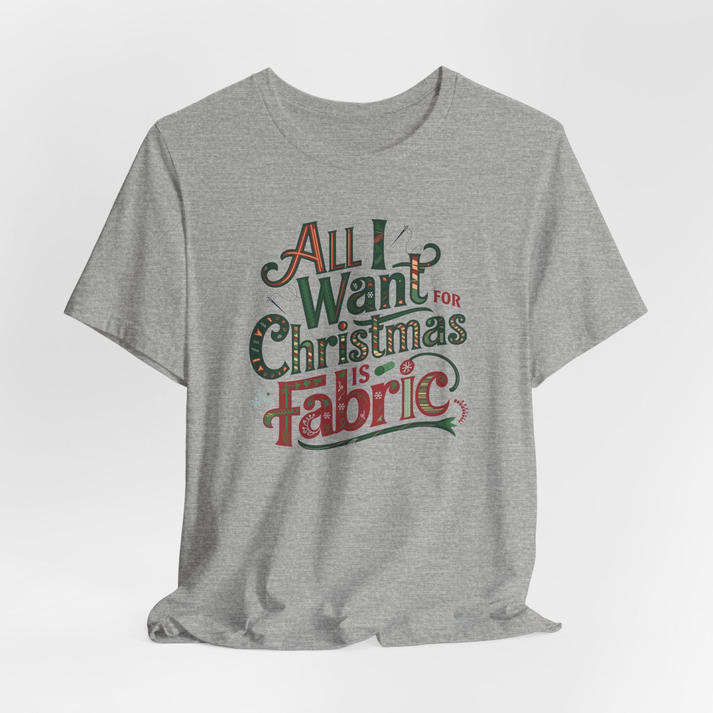 An Athletic Heather festive quilting christmas T-shirt featuring the phrase "All I Want for Christmas is Fabric," with fun sewing and quilting accents like needles and threads swirling around the text.