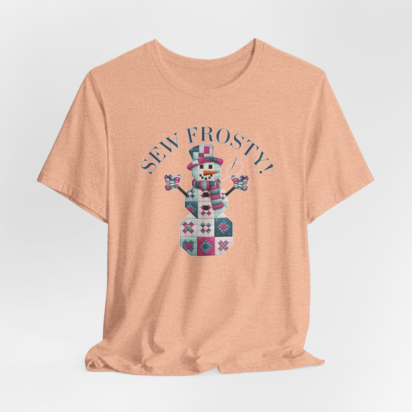 A Heather Peach christmas quilting t-shirt featuring cute snowman made of patchwork quilt blocks with the phrase "Sew Frosty" above, holding a needle to highlight the quilting theme.