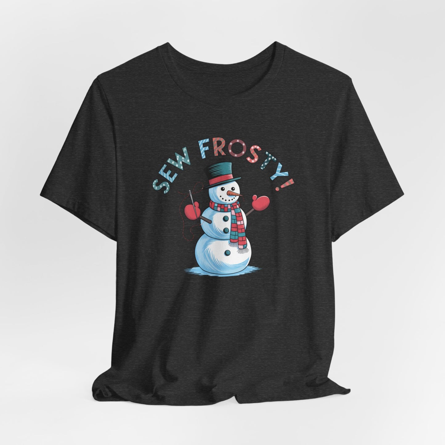 A Dark Grey Heather christmas quilting t-shirt featuring cheerful snowman design holding a sewing needle, with the phrase "Sew Frosty" in playful, winter-themed lettering. The snowman is wearing a scarf and mittens, ready for holiday sewing fun.