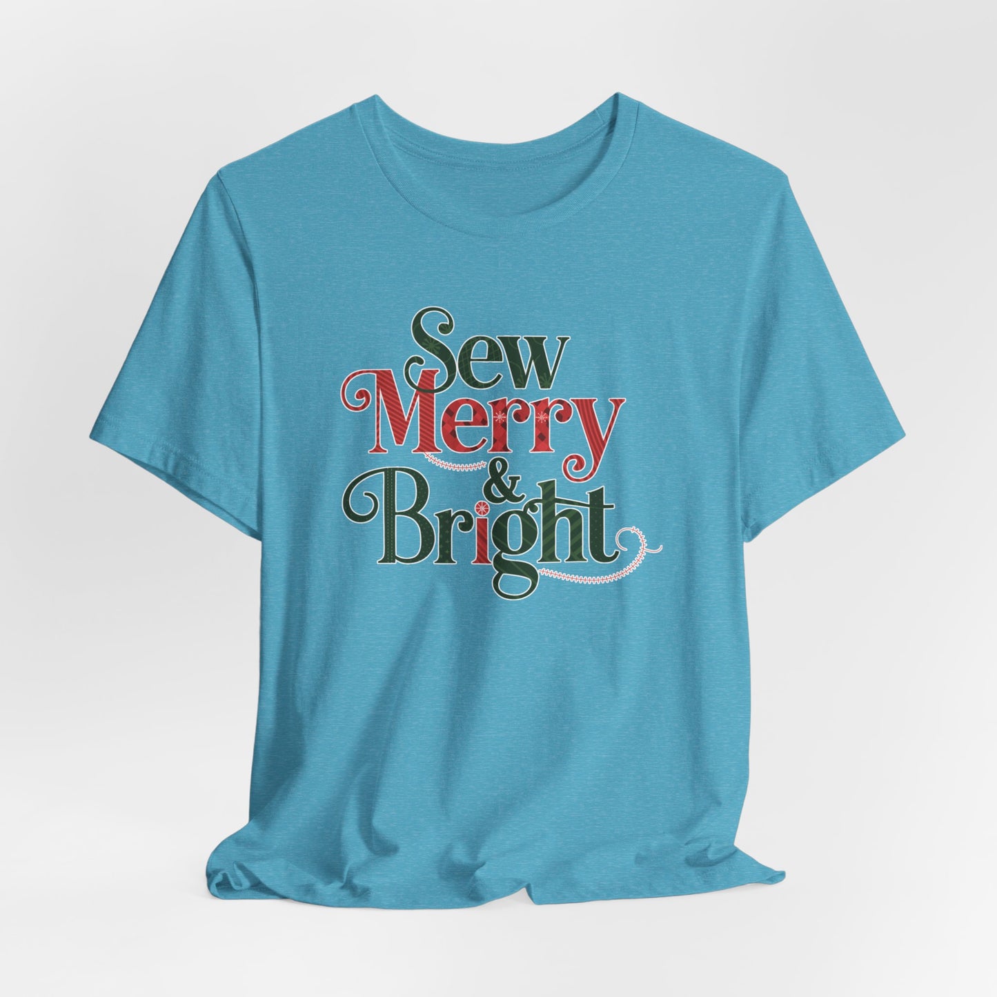 A Heather Aqua t-shirt with the phrase "Sew Merry & Bright," incorporating sewing-inspired elements and holiday-themed accents, such as stitching lines and festive patterns.