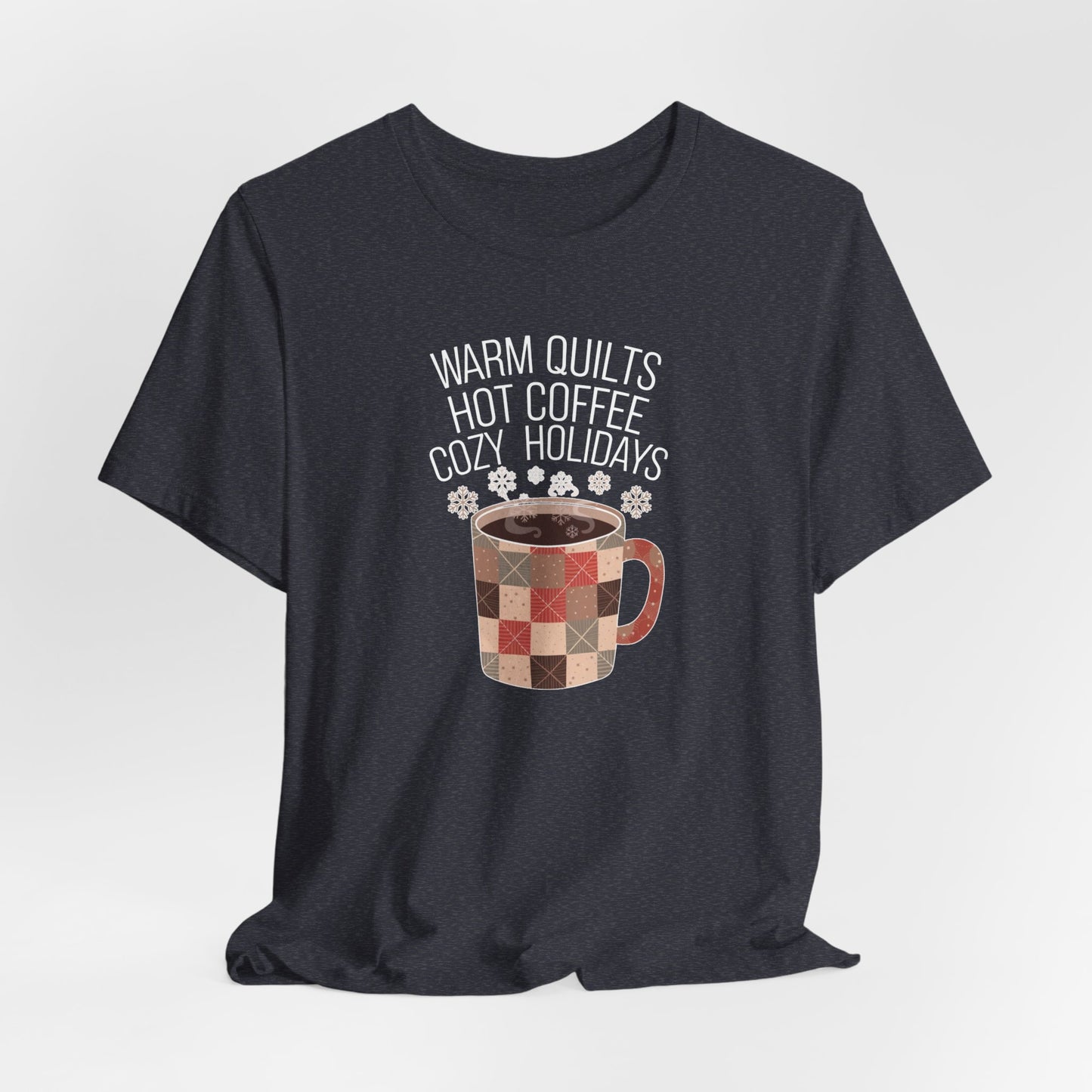 A Heather Navy christmas quilting t-shirt featuring a cozy patchwork quilt-themed coffee mug, surrounded by snowflakes, with the phrase "Warm Quilts, Hot Coffee, Cozy Holidays" above the mug, celebrating the warmth of quilts and coffee during the holiday season.