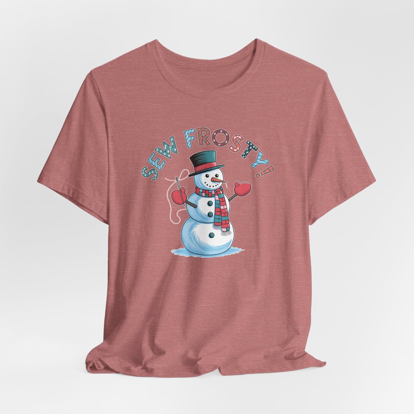 A Heather Mauve christmas quilting t-shirt featuring cheerful snowman design holding a sewing needle, with the phrase "Sew Frosty" in playful, winter-themed lettering. The snowman is wearing a scarf and mittens, ready for holiday sewing fun.