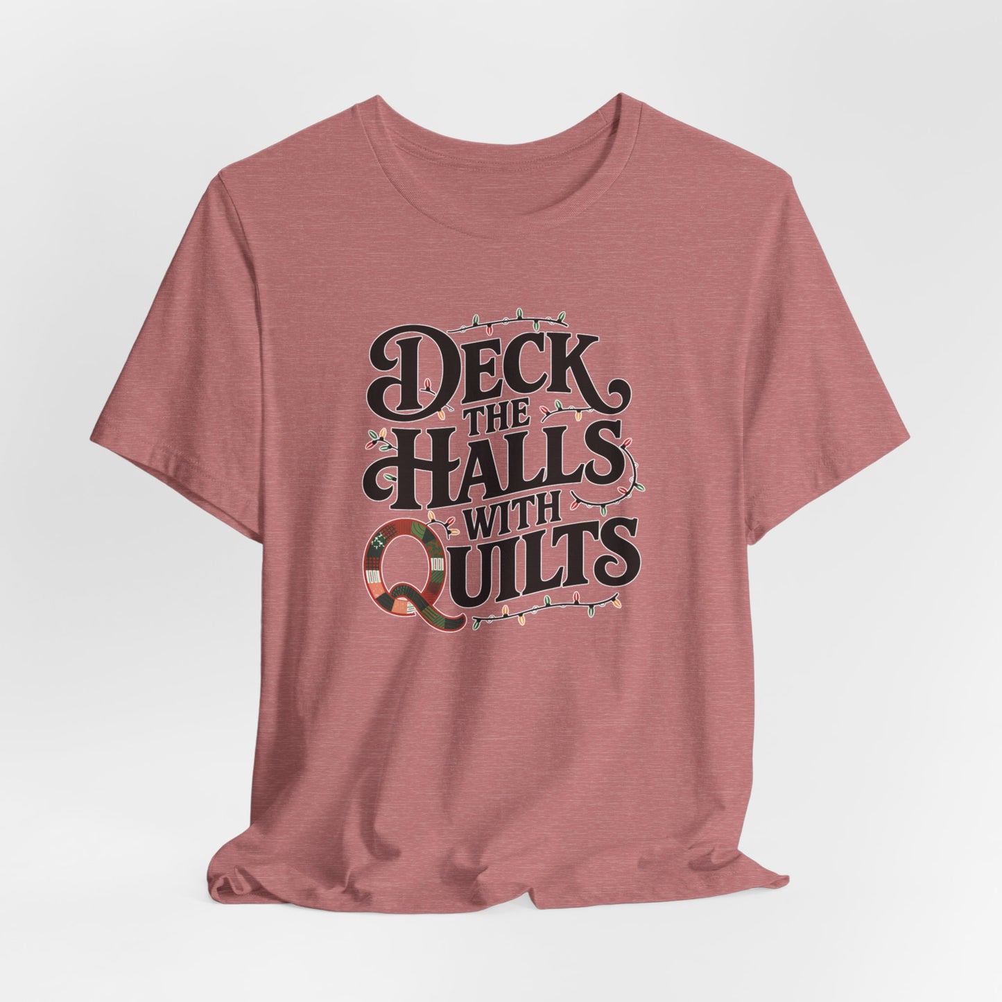 A Heather Mauve christmas quilting t-shirt featuring the phrase "Deck the Halls with Quilts," adorned with holiday lights and quilting-inspired elements, including a quilted 'Q' for a humorous touch.