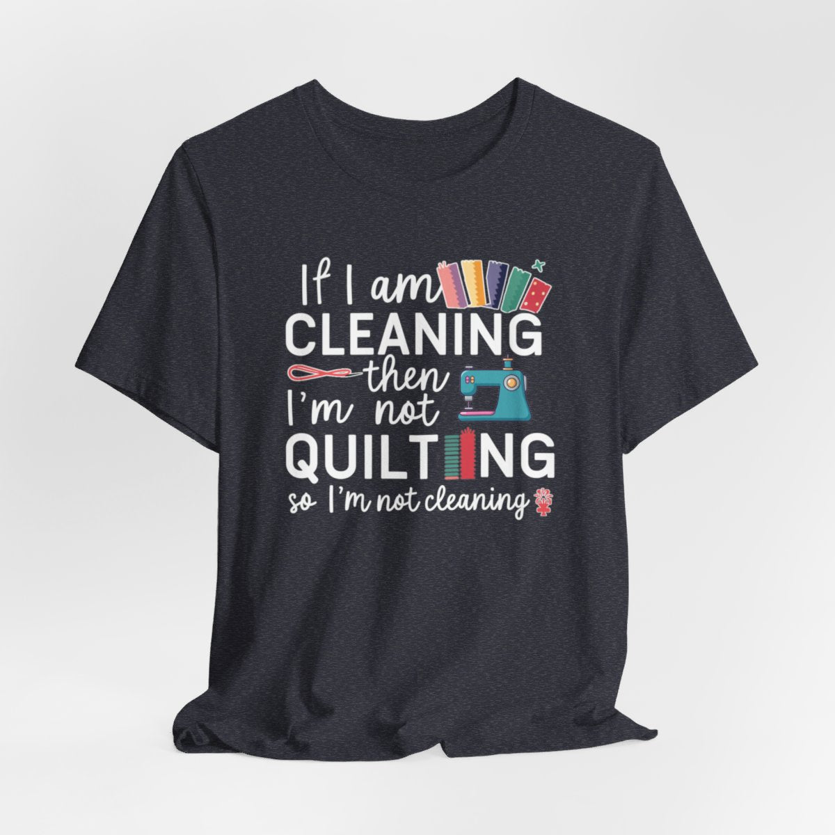 A Heather Navy funny quilting T-Shirt with the phrase If I am Cleaning then I'm not Quilting in a bold and cheerful font with images of quilting icons and supplies